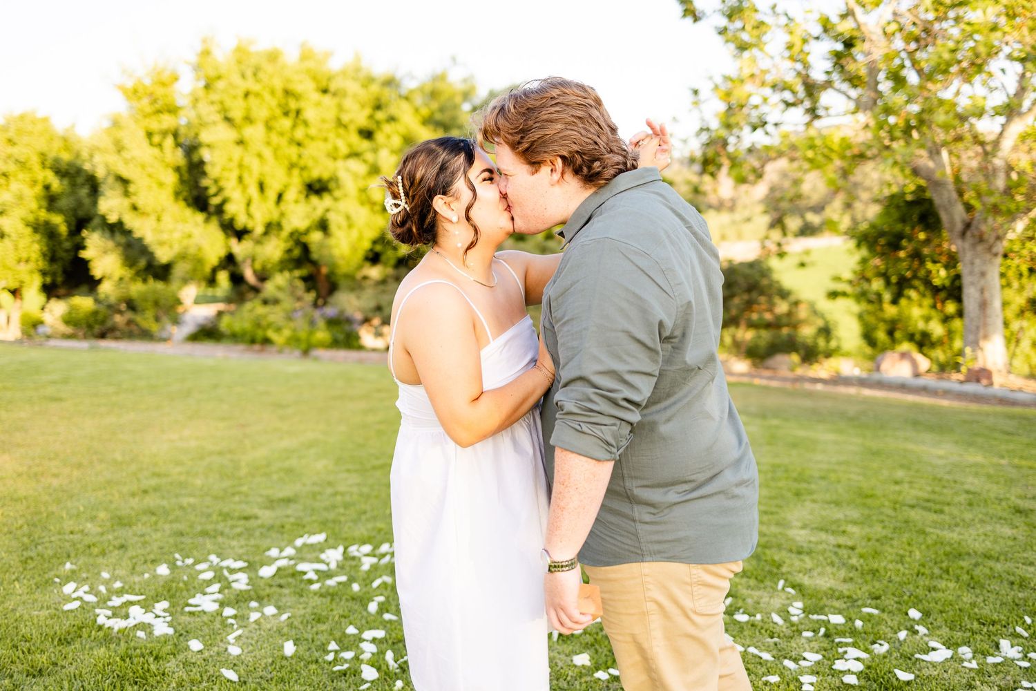 A tender moment shared between two people amid scattered white flowers at sunset.