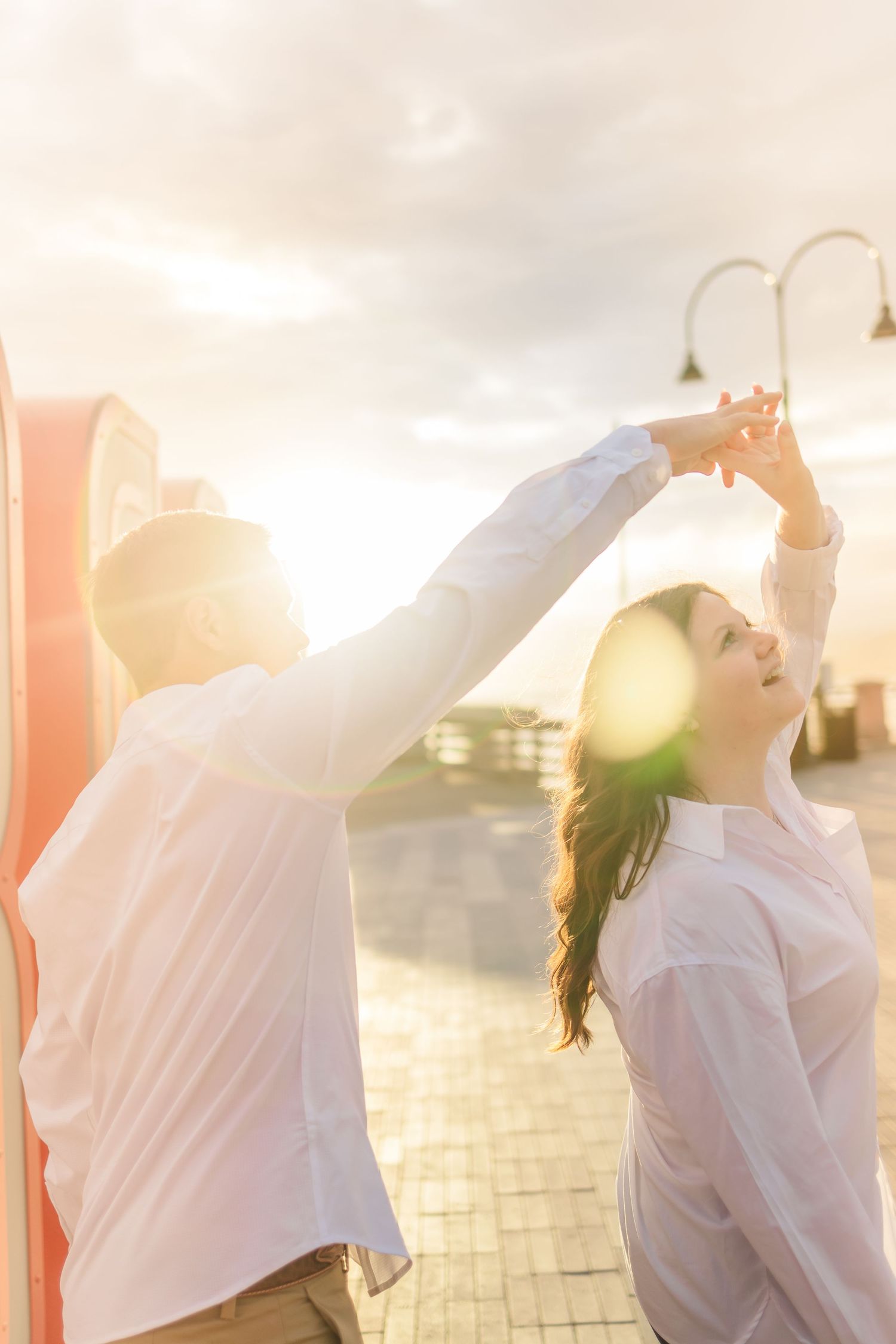 Couple dances with raised arms against sunset sky and outdoor signage.