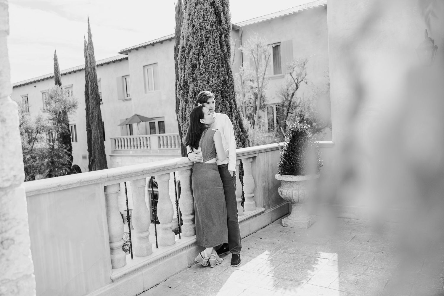 A black and white vintage photograph showing a couple on a Mediterranean-style terrace with cypress trees in the background.
