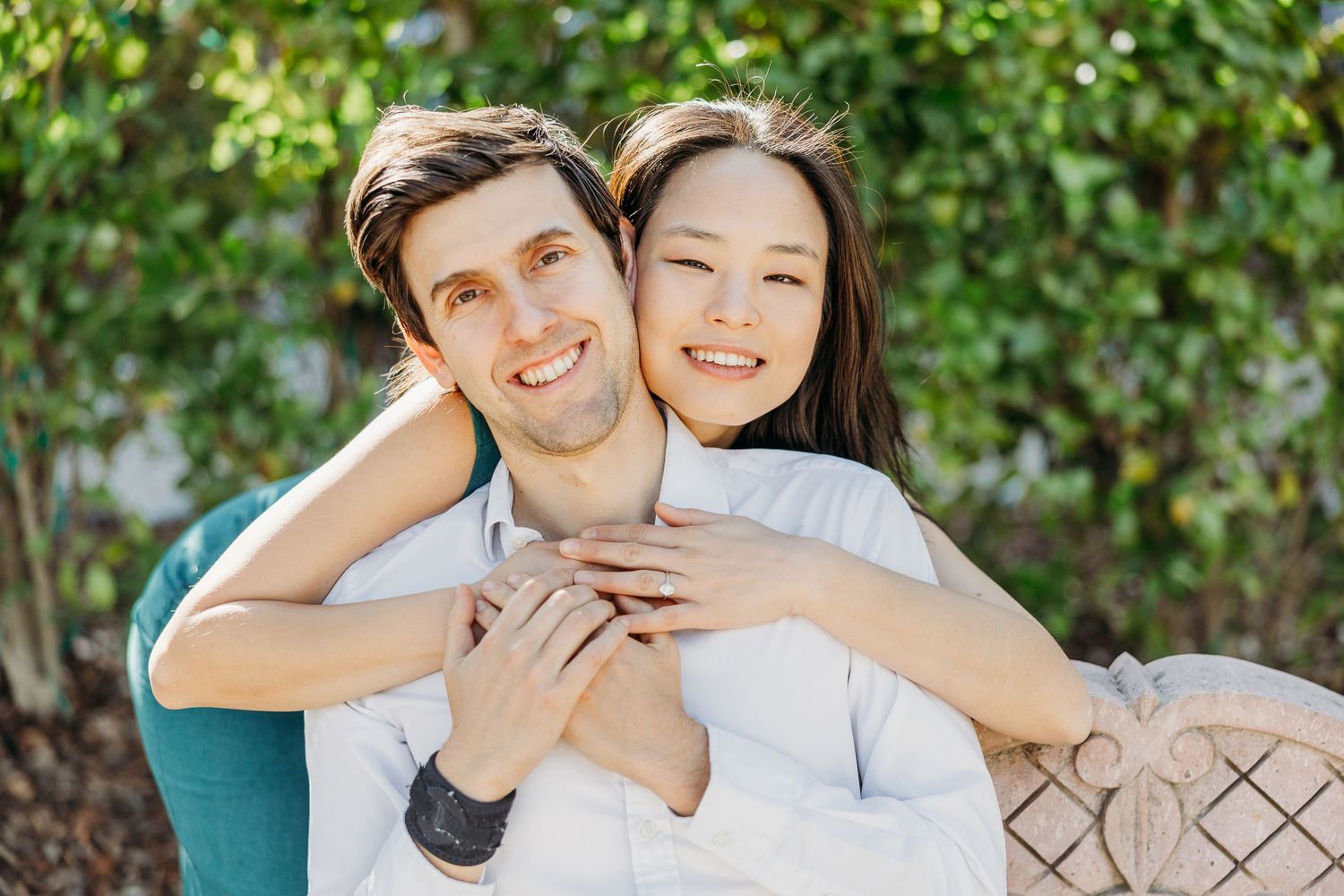 A happy couple sharing a joyful embrace outdoors against lush green foliage.