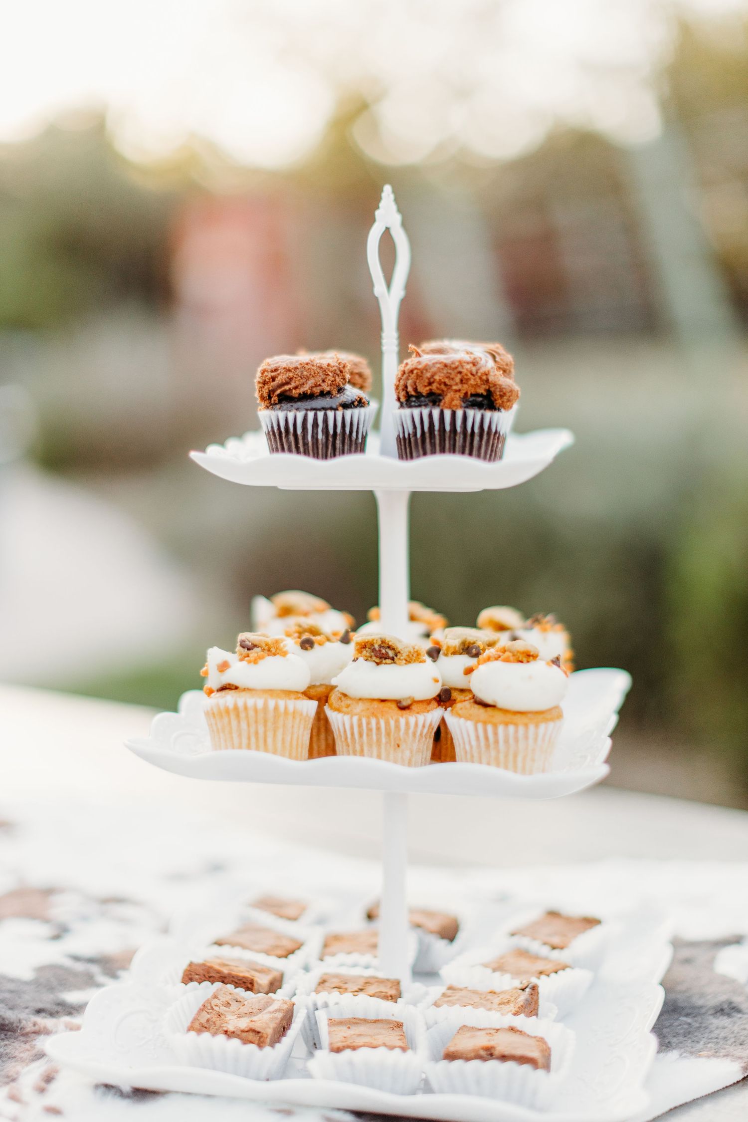 Two-tier dessert stand displaying chocolate cupcakes and pastries at outdoor event.