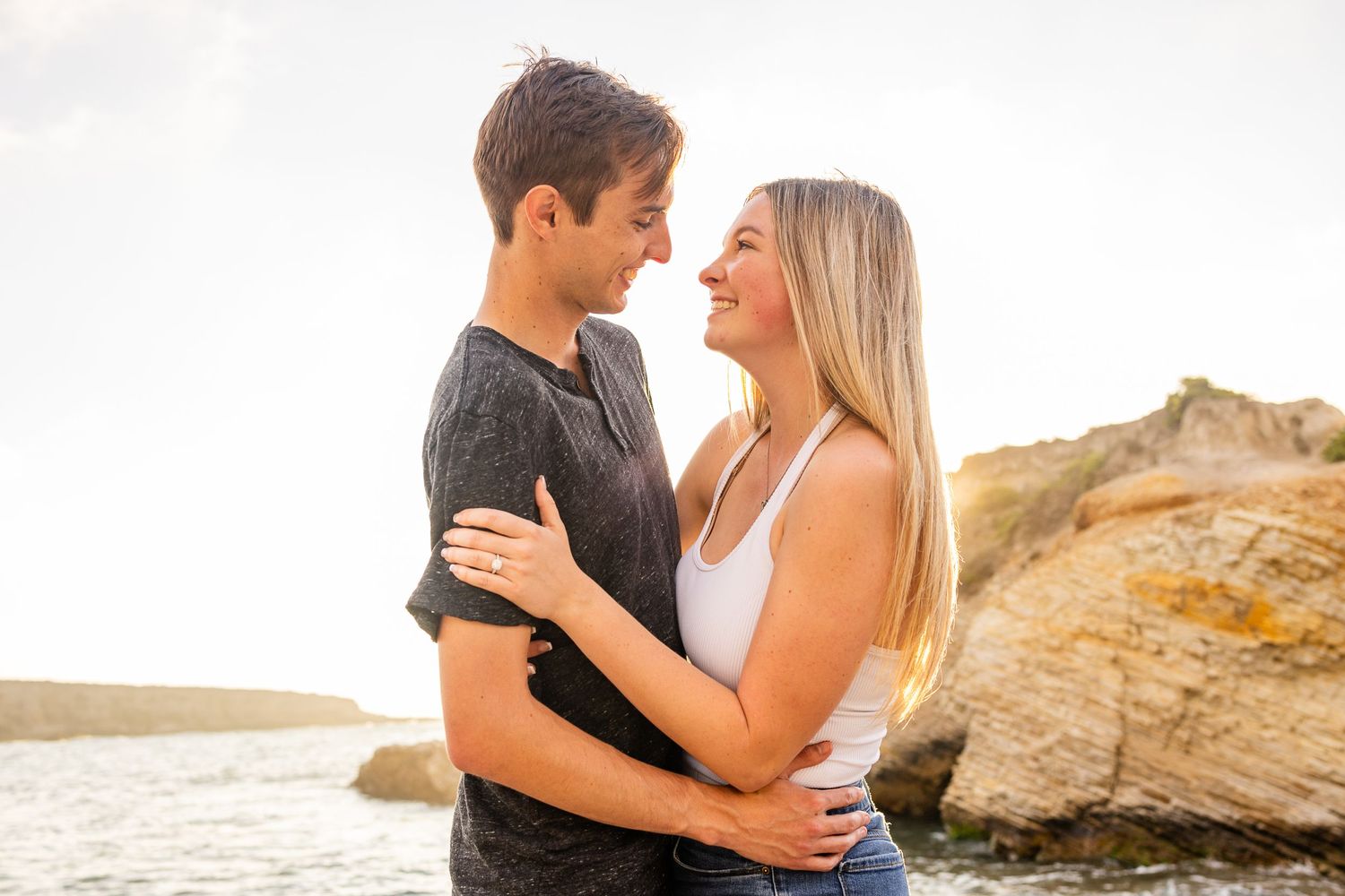A loving couple shares an intimate moment on a beach with golden sunlight.