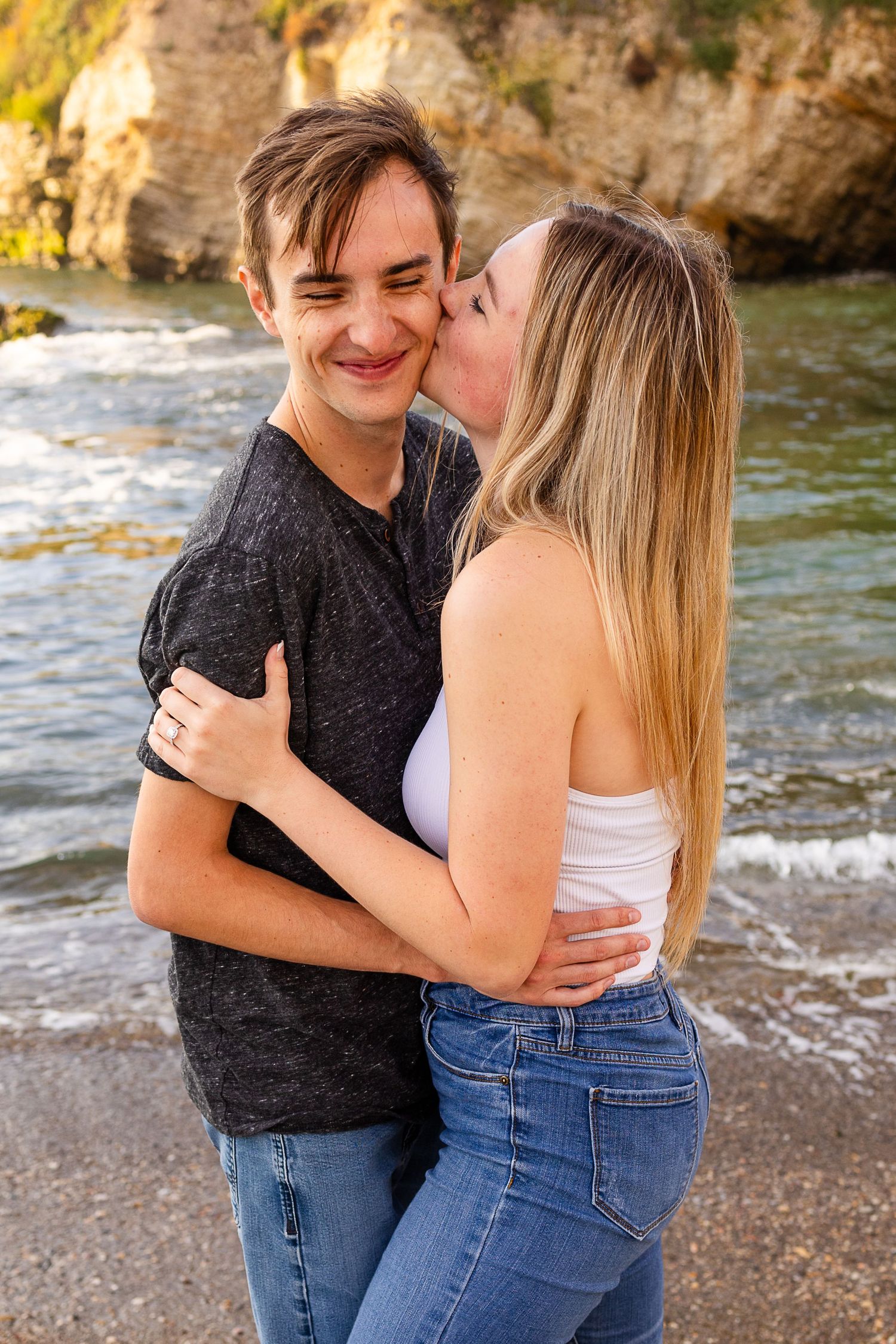 An intimate moment shared between a couple on a rocky beach with cliffs behind them.
