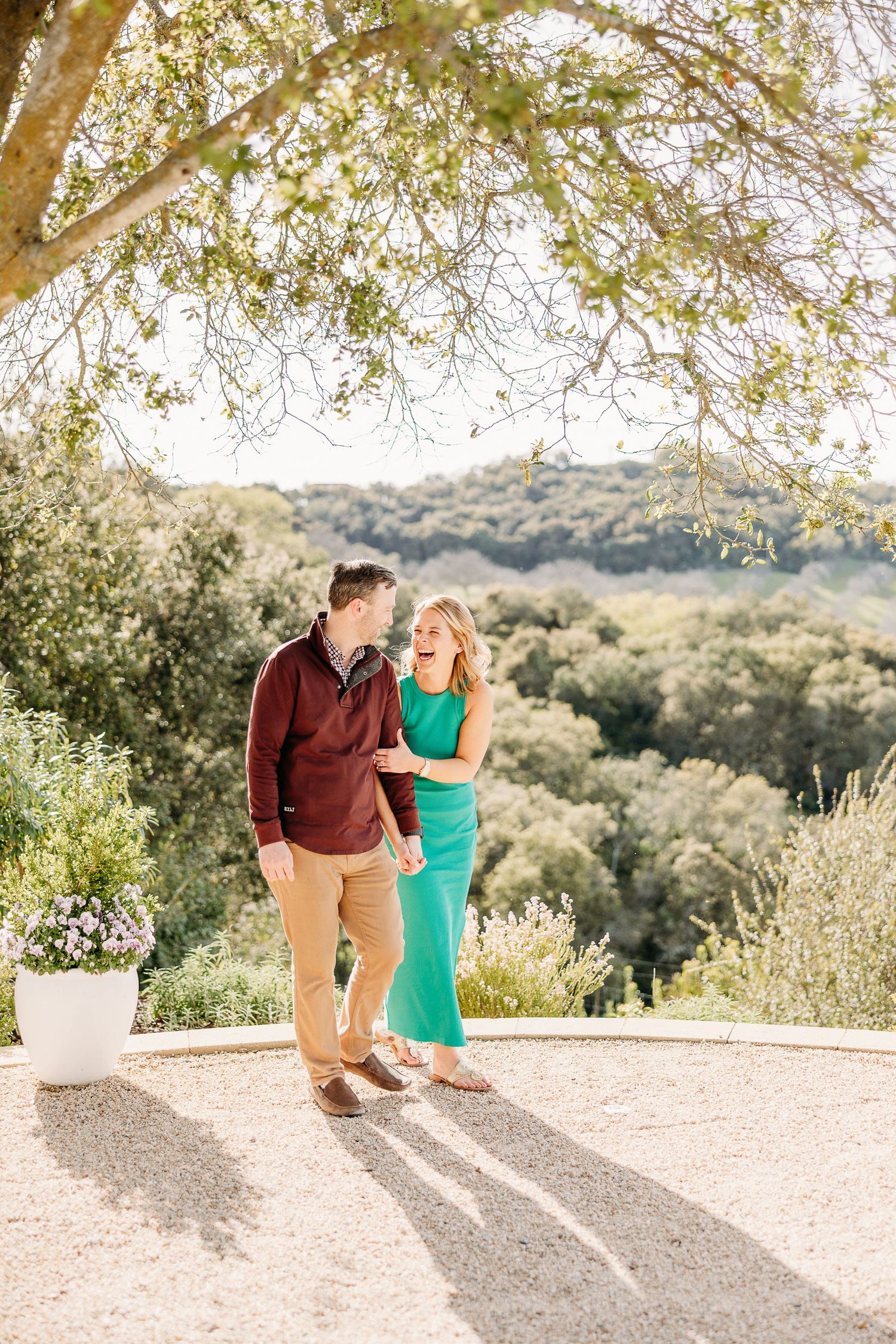 A couple shares romantic moments during their outdoor photoshoot on a sunny patio surrounded by trees.