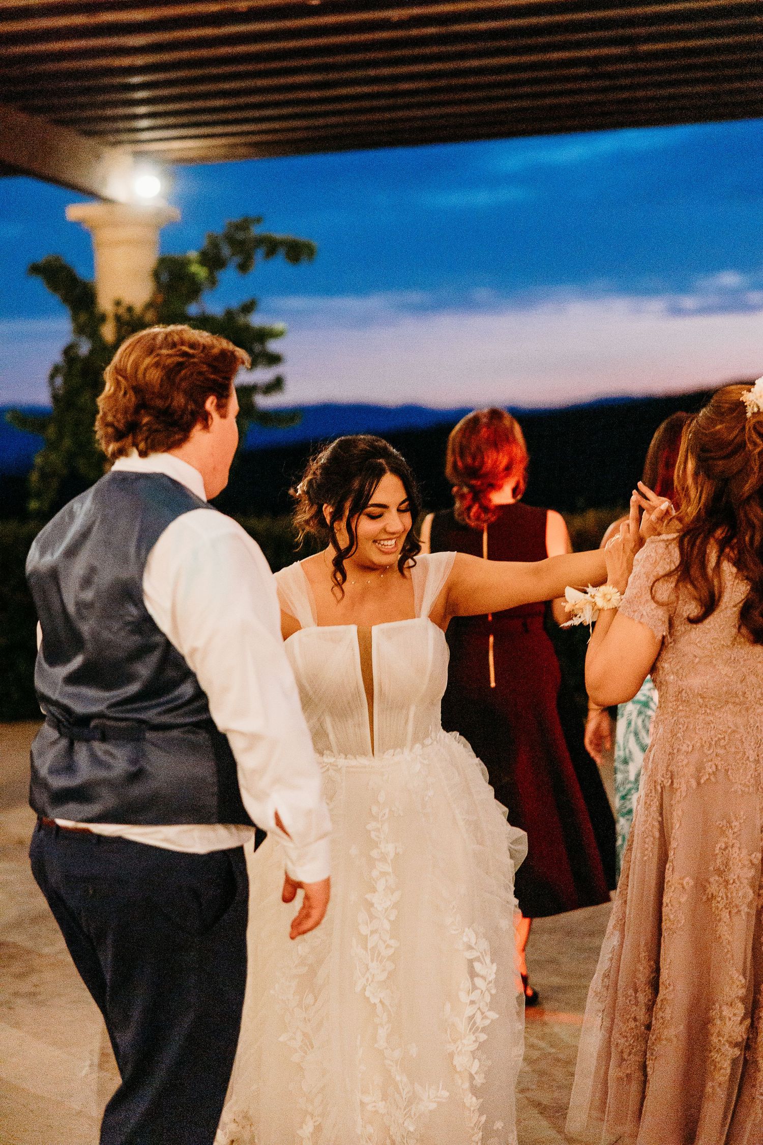 Newlyweds dancing with guests during sunset at an outdoor wedding reception.