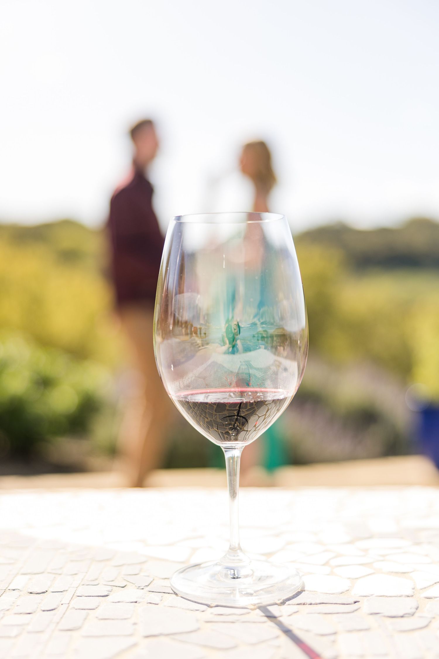 Wine glasses filled with white wine sit on an outdoor table with blurred natural background.