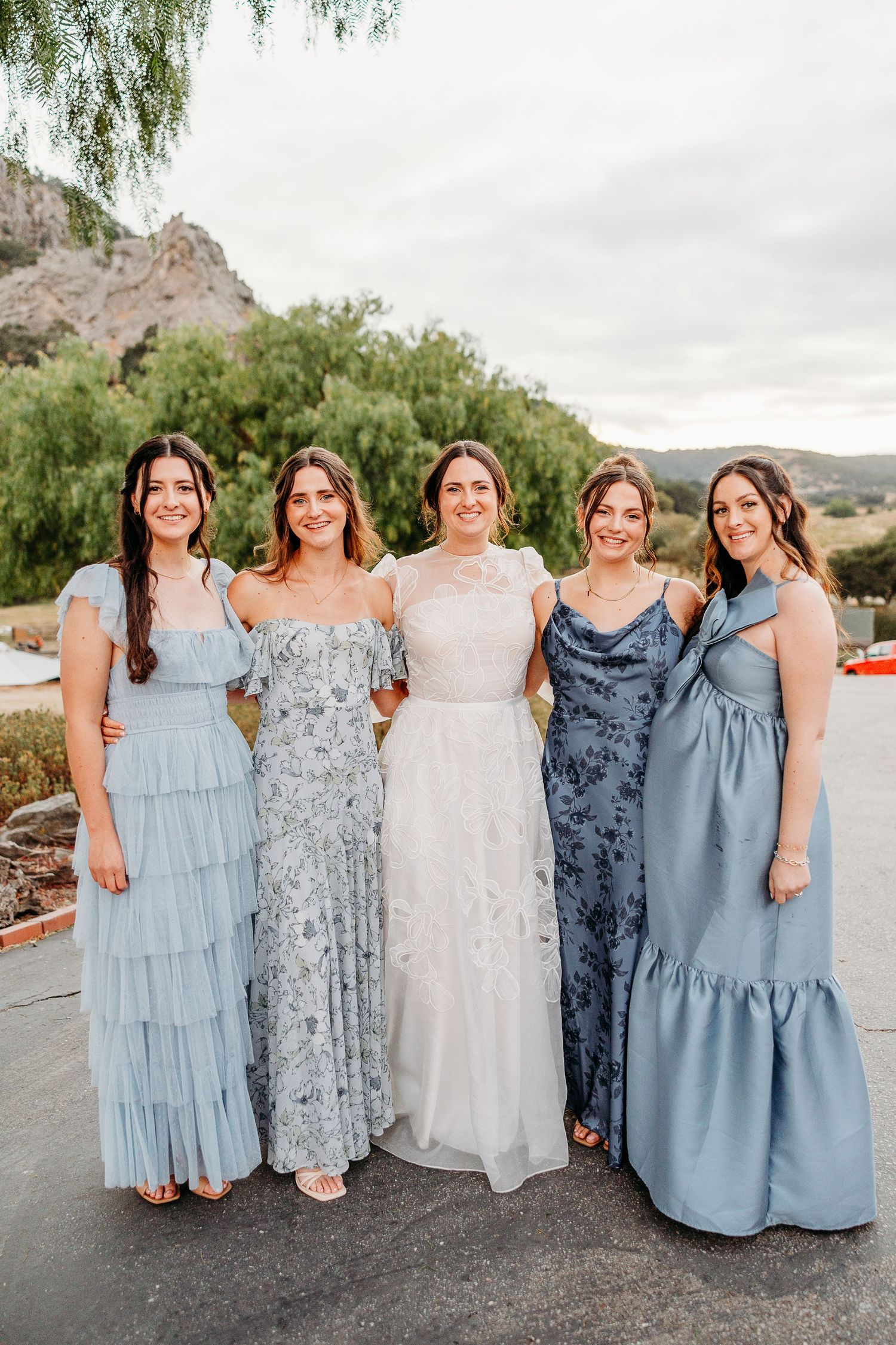 Bridal party in coordinating blue and floral dresses posing against mountain landscape at San Luis Obispo Holland Ranch.