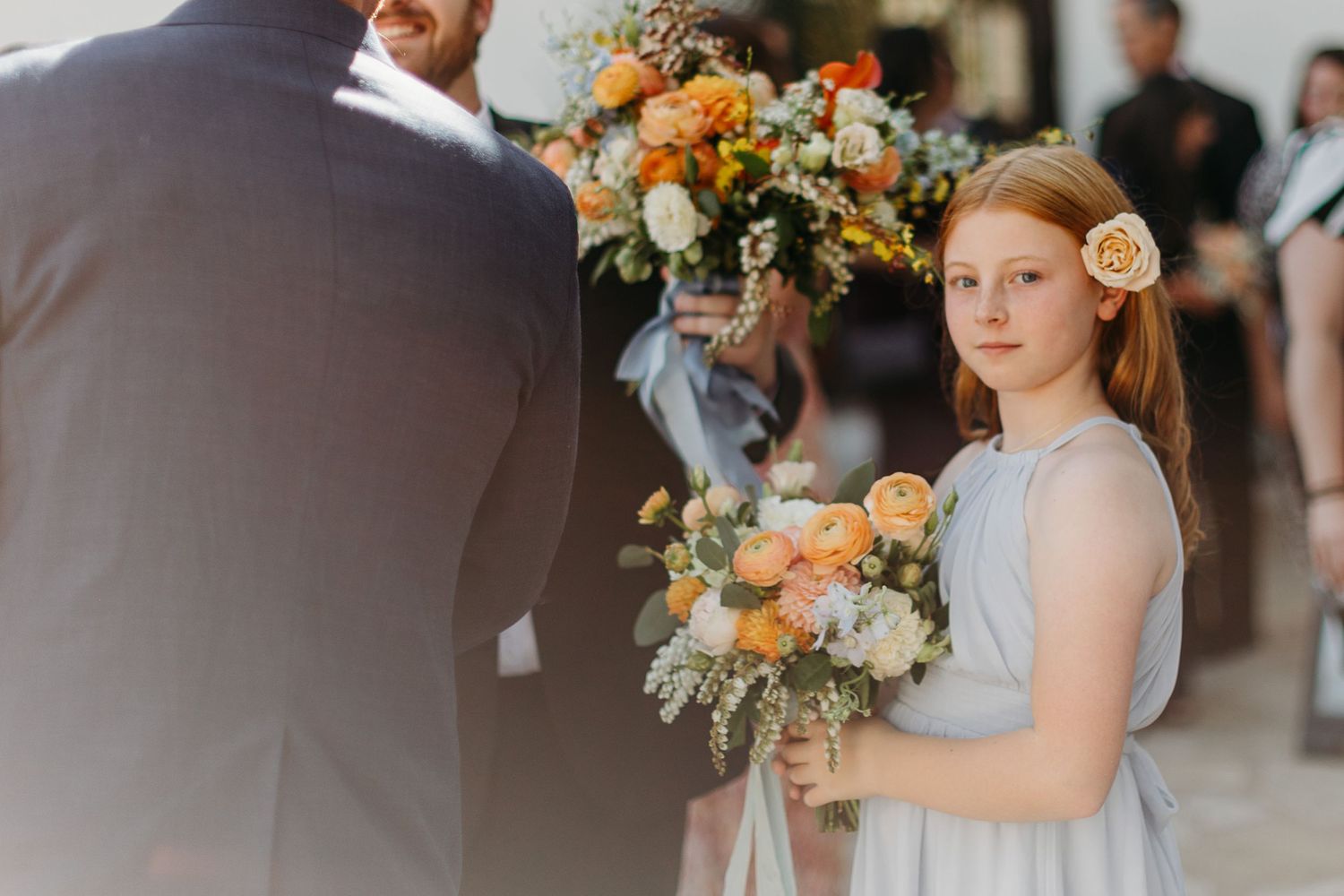 Young attendant holding peach and orange floral bouquet at wedding at SLO Mission