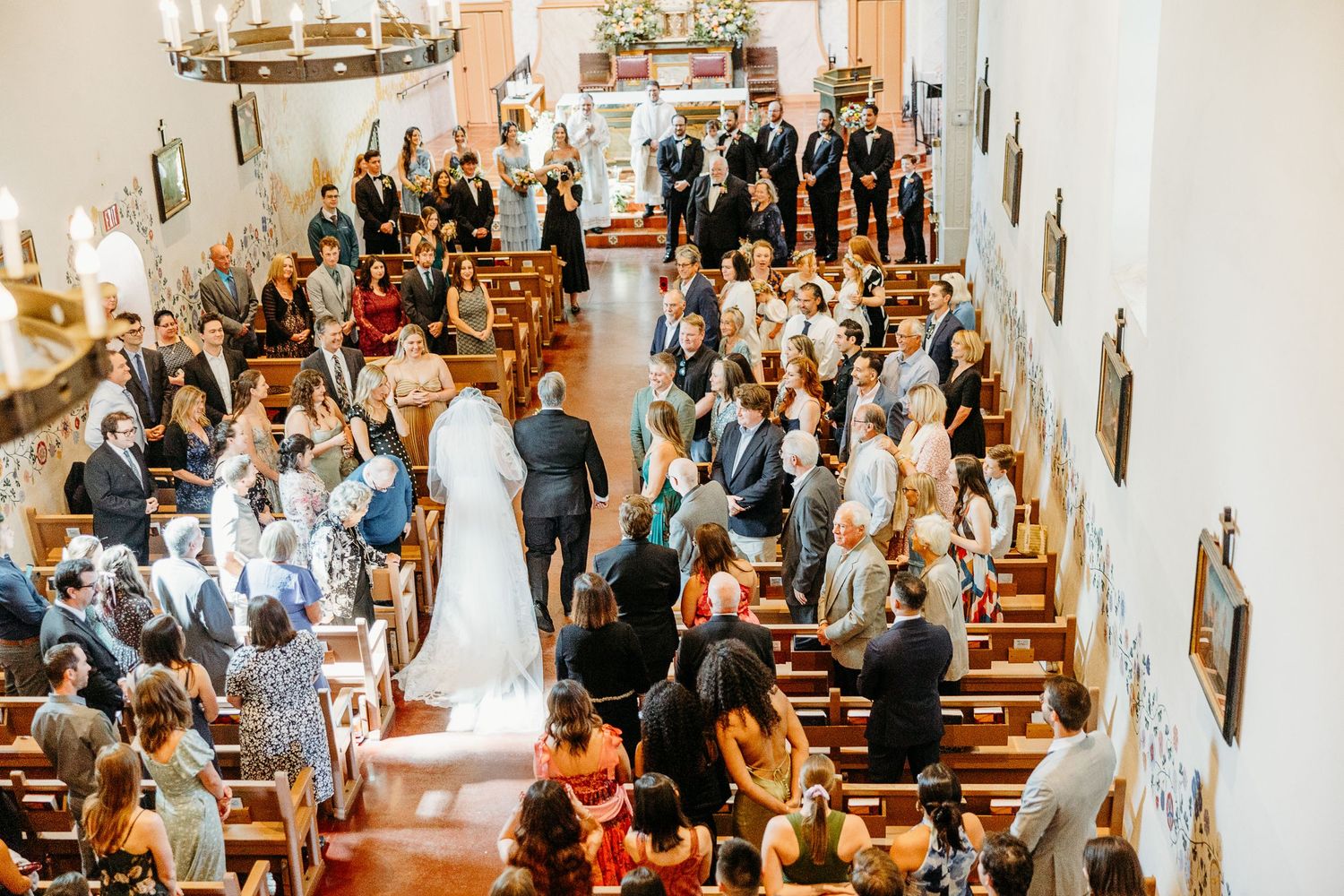 Overhead view of wedding ceremony in traditional white church filled with guests in pews.