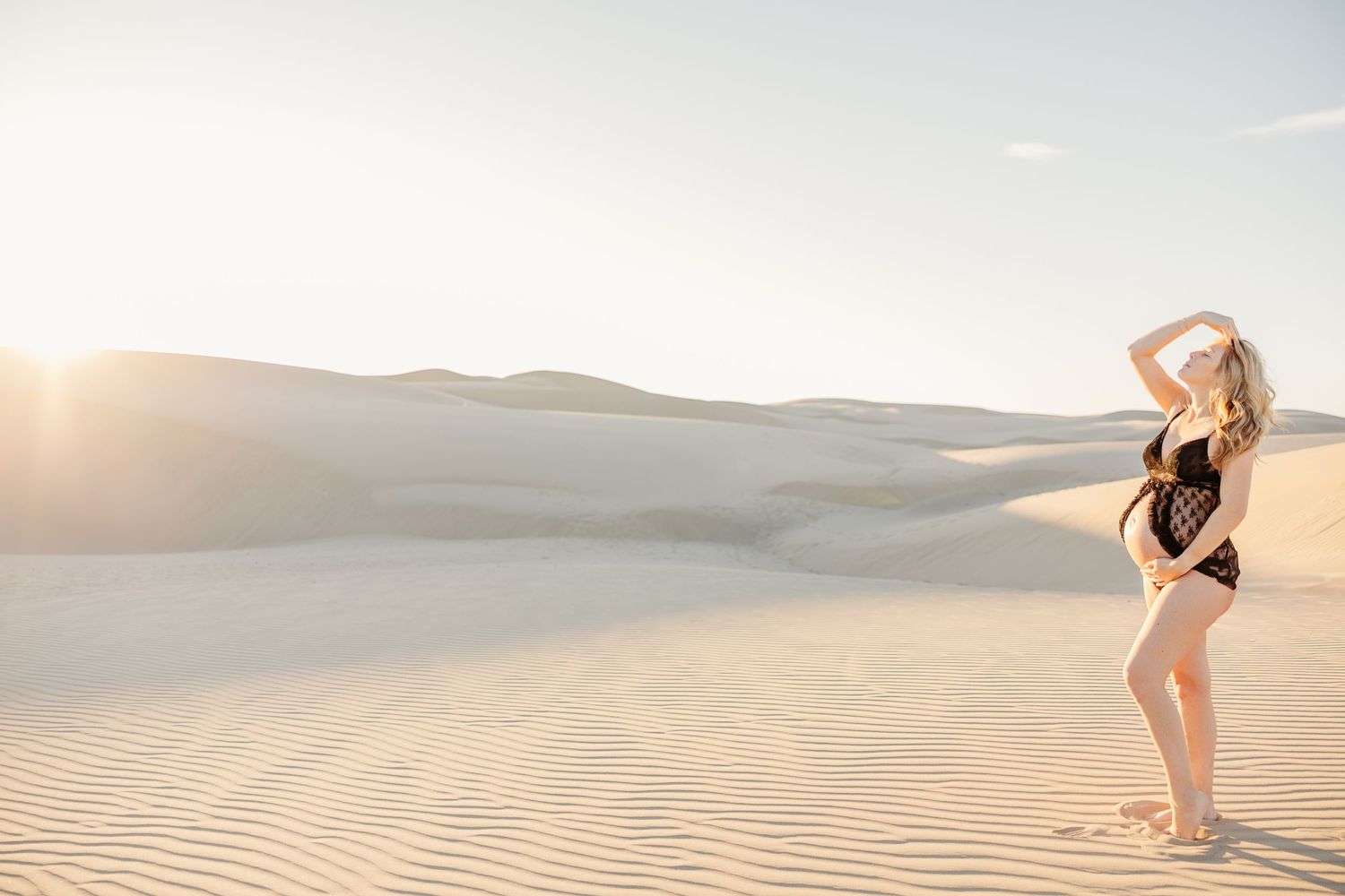 Silhouette of someone standing on sand dunes at sunset wearing a black swimsuit.