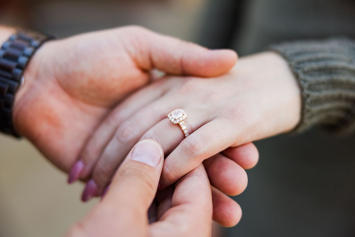 Close-up shot of engagement ring being placed on hand against neutral background.
