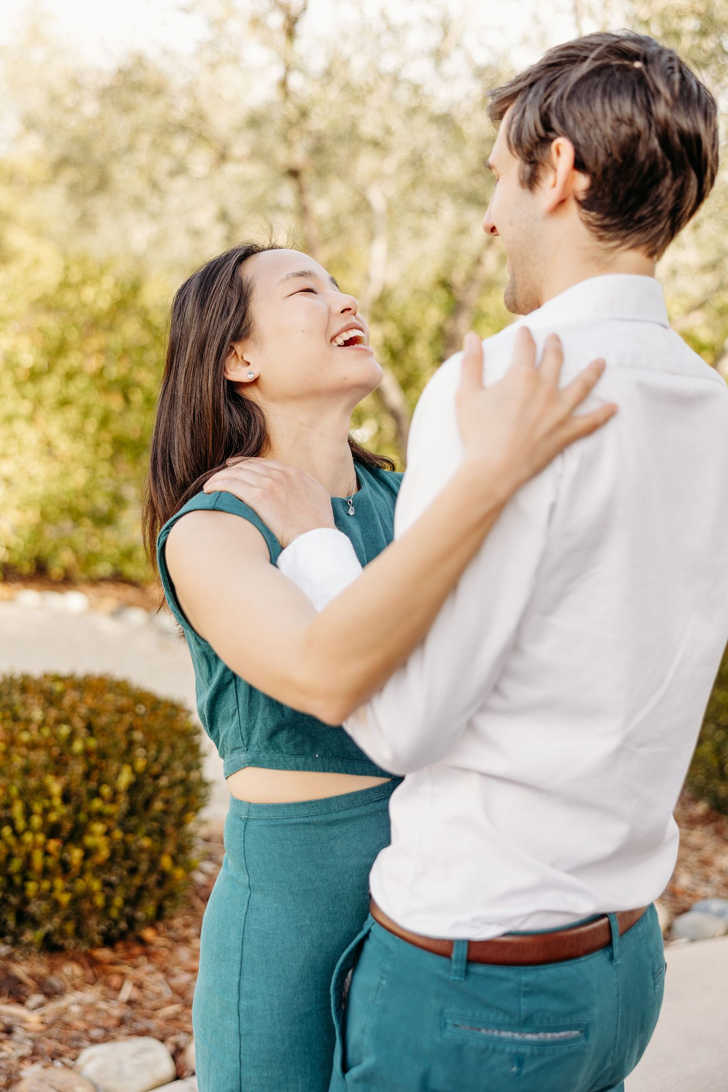 A joyful couple sharing a laugh while embracing outdoors in warm sunlight.