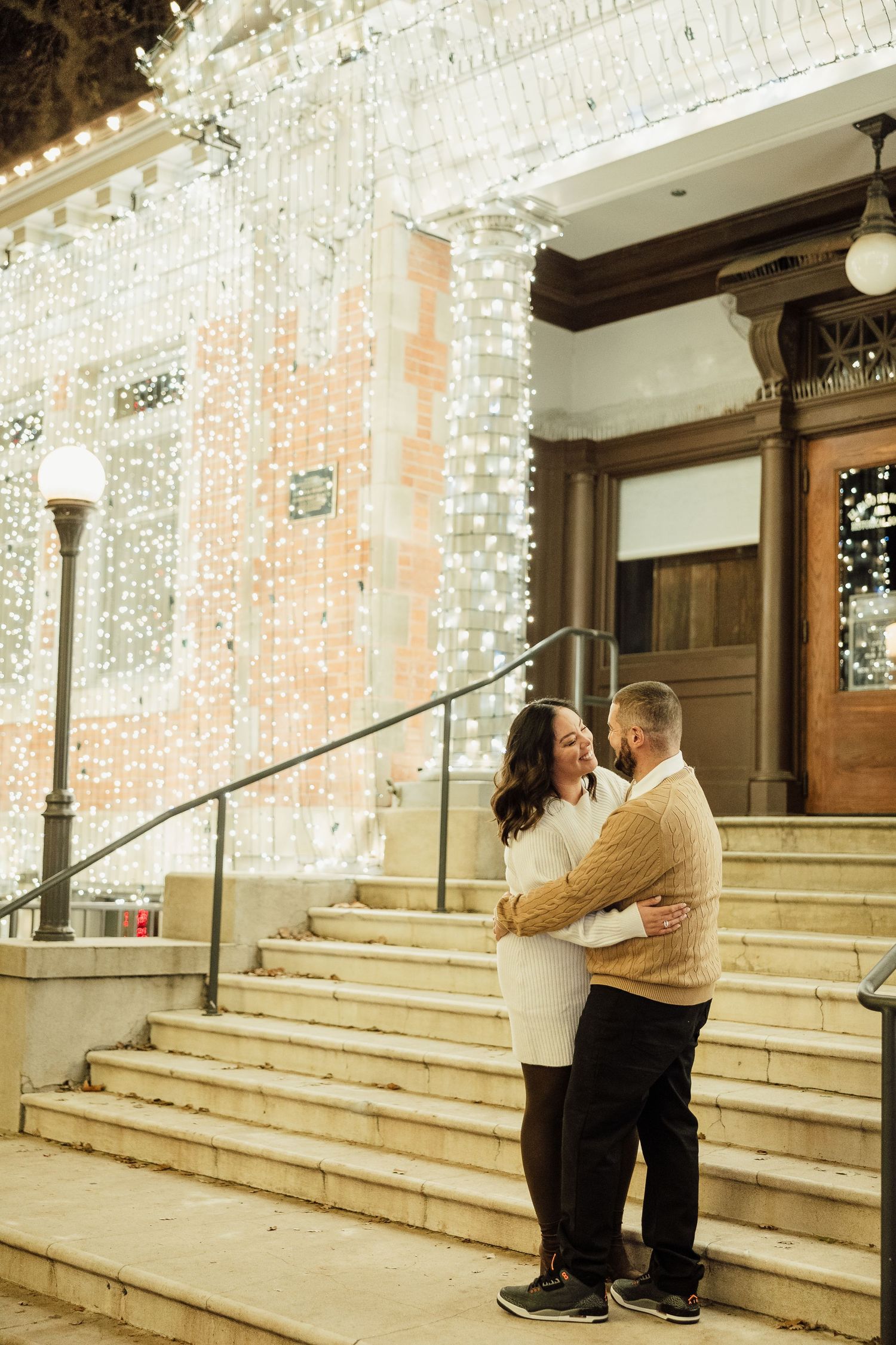 A romantic proposal moment unfolds on stone steps decorated with twinkling string lights in an elegant indoor setting.