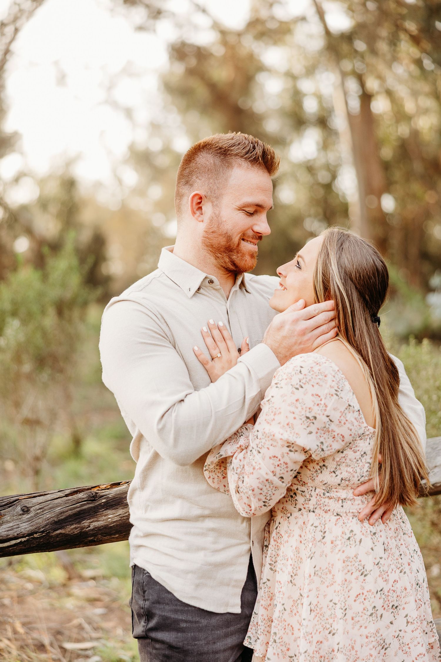 Tender moment between couple against rustic wooden fence backdrop.