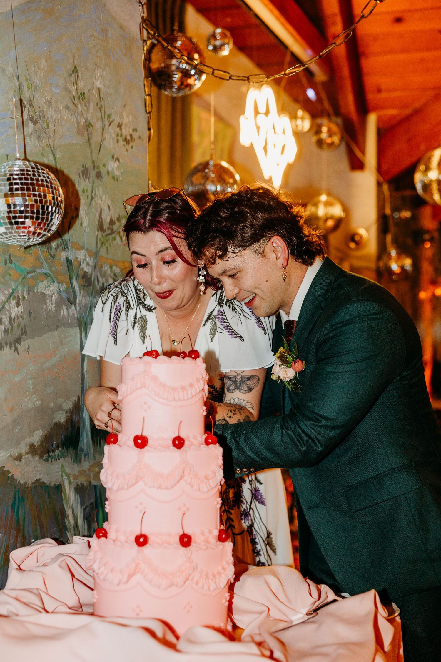 Couple sharing a moment with their pink wedding cake decorated with red cherries.
