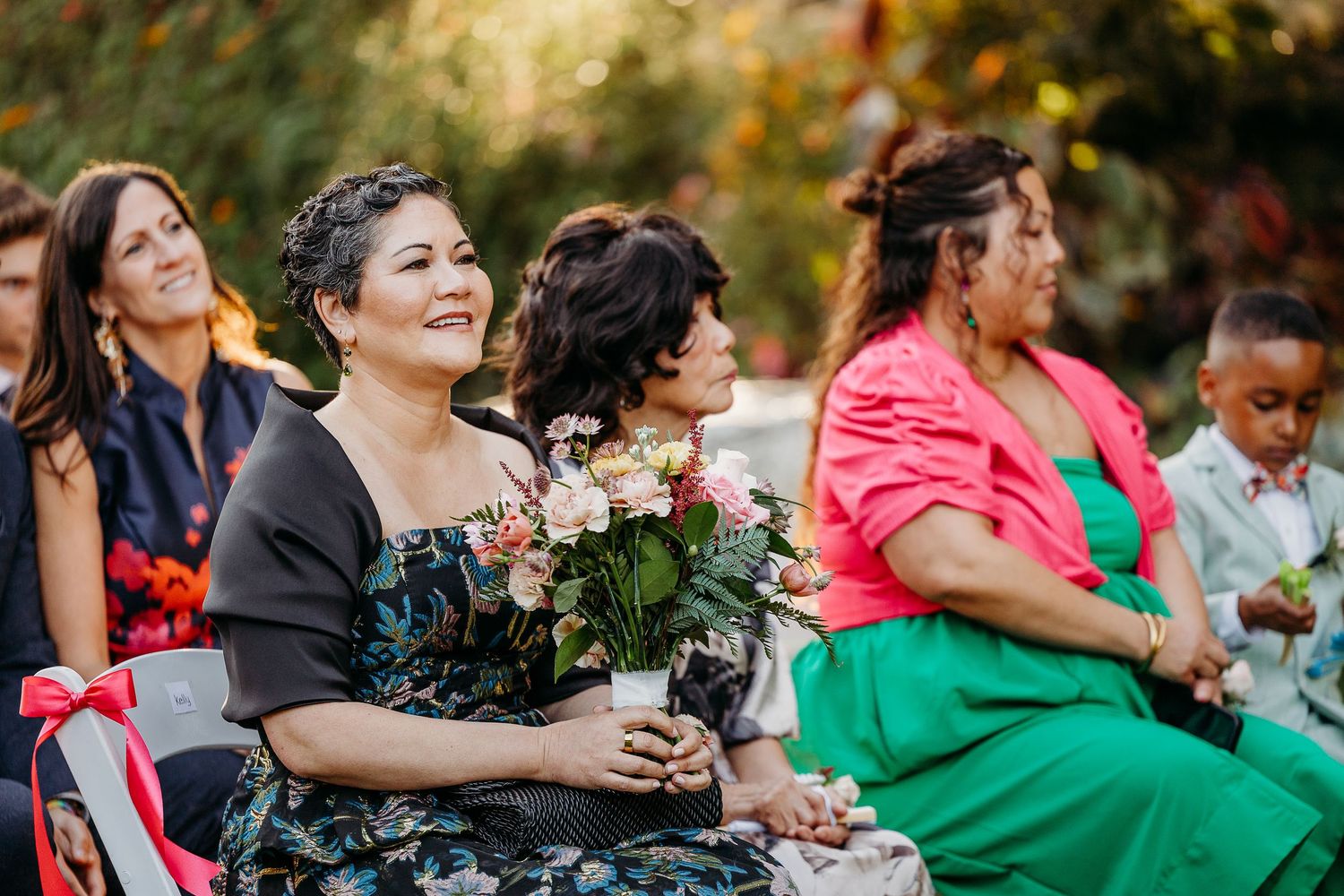 Wedding guests seated outdoors holding bouquets during autumn ceremony.