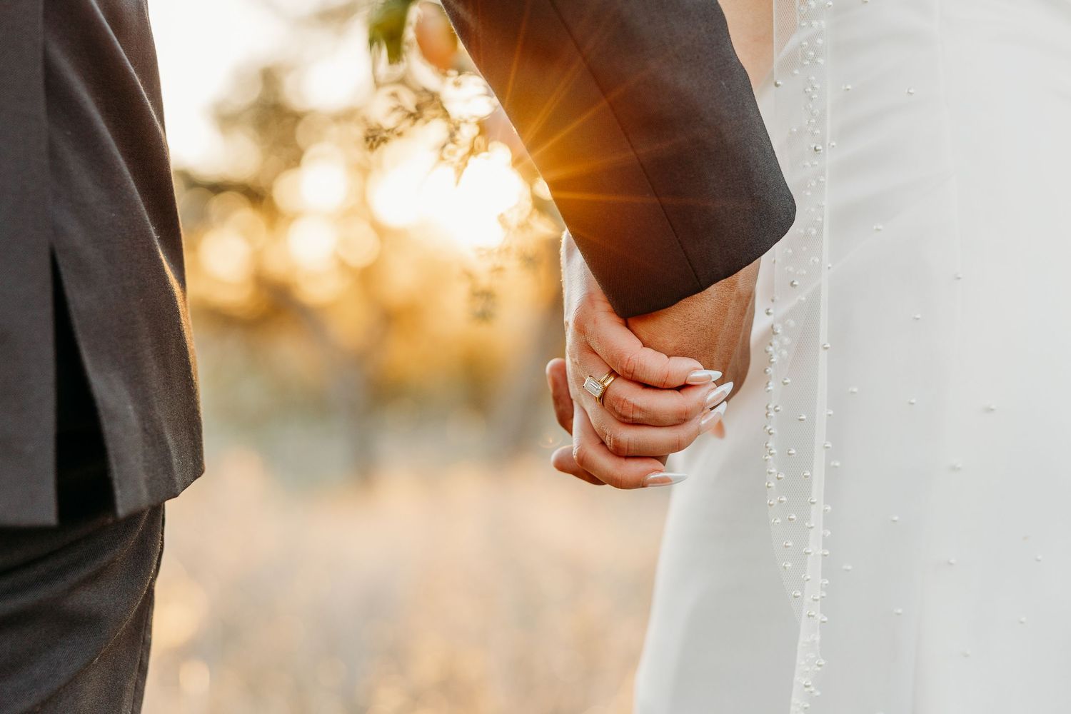 A couple holding hands at sunset with sunlight streaming through their clasped fingers during a wedding ceremony.