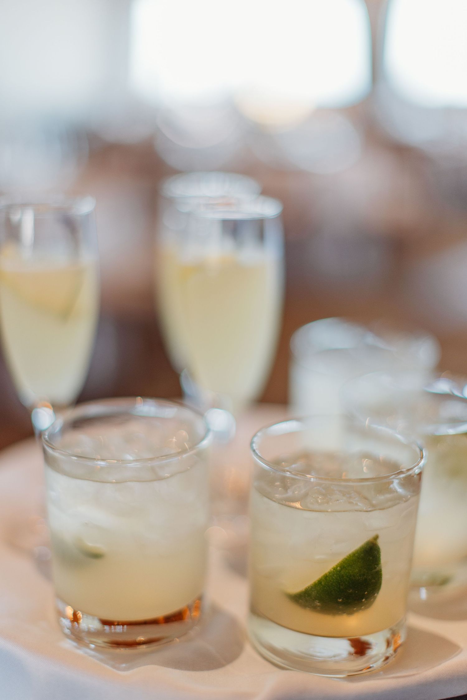 Row of cocktail glasses filled with clear drinks garnished with lime wedges on a wooden surface.