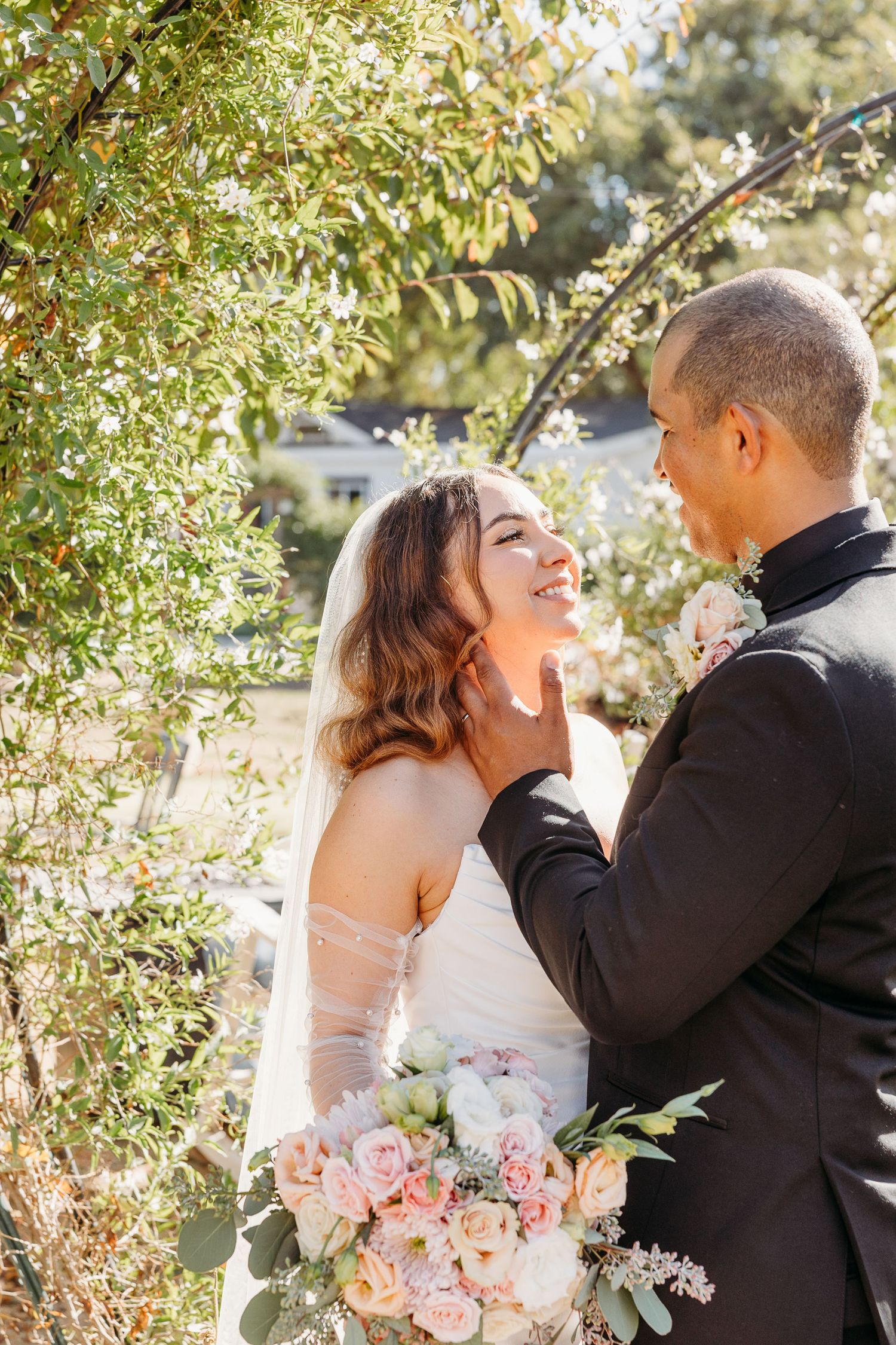 Romantic wedding couple embraces under blooming trees during golden hour portrait session.