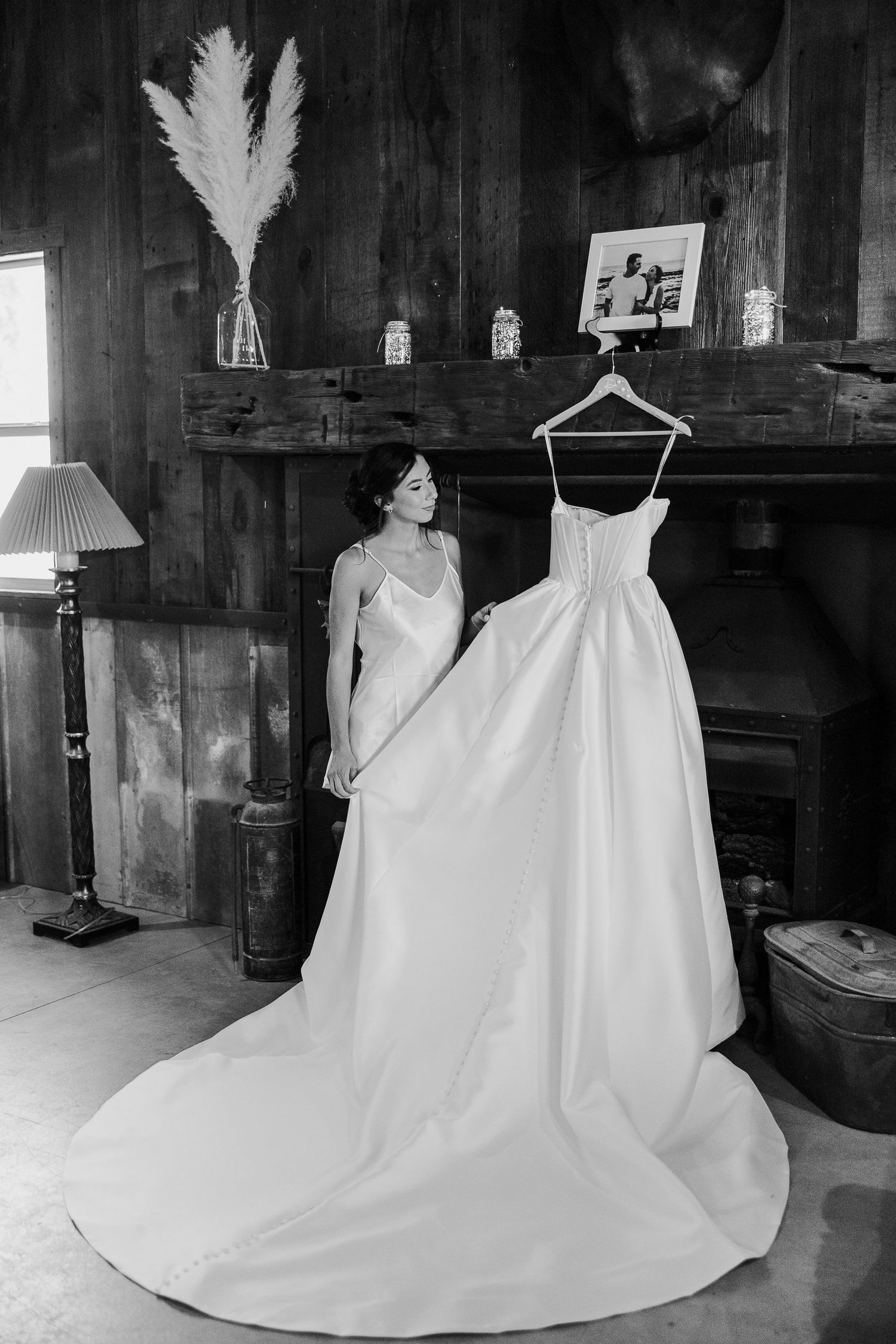 A white wedding dress with a long train and feather details is displayed in a rustic wooden room.
