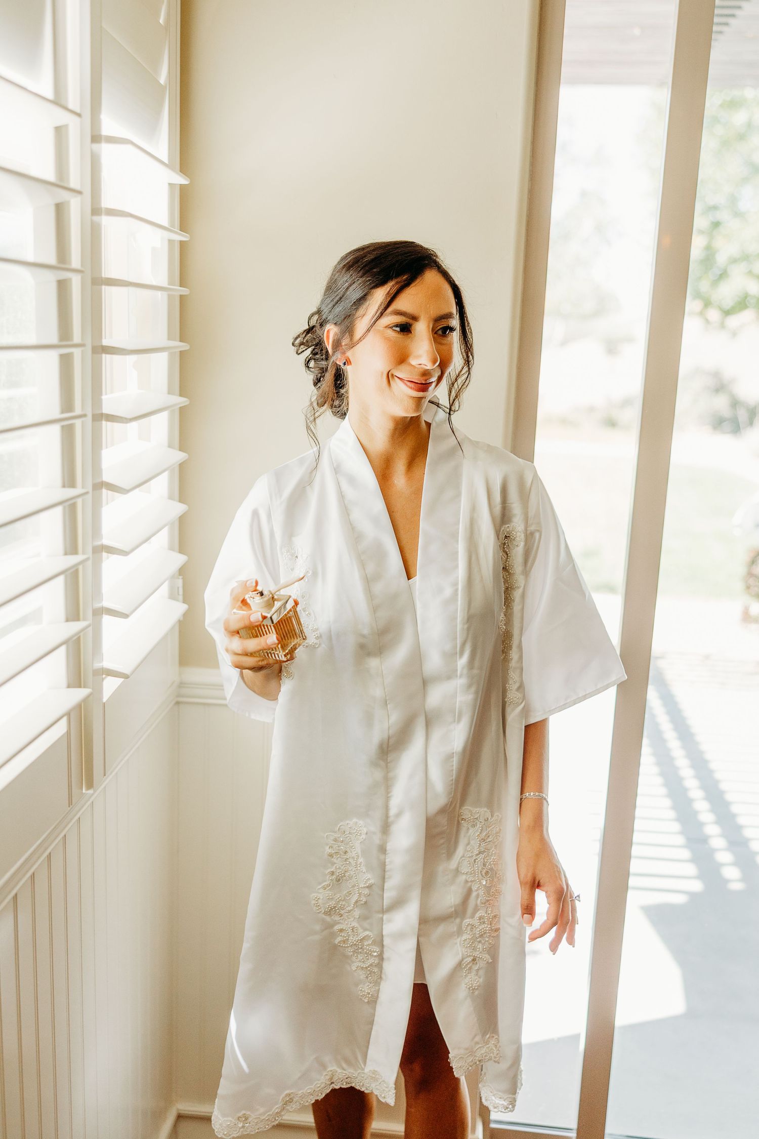 Woman in white robe getting ready in bright sunlit room with window light creating beautiful shadows.
