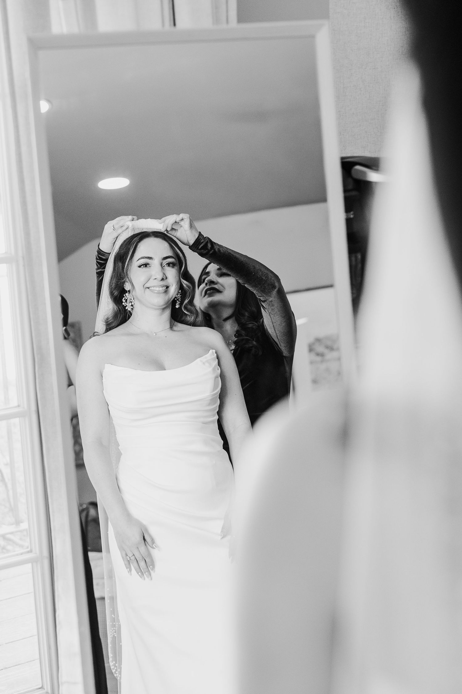 Bride in white wedding dress poses near window in bright interior setting.