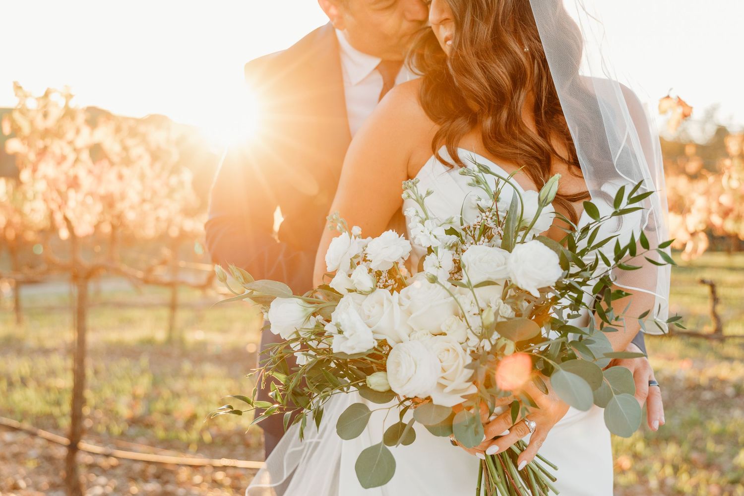 Sunlit wedding bouquet with white flowers and greenery held against a golden sunset background.