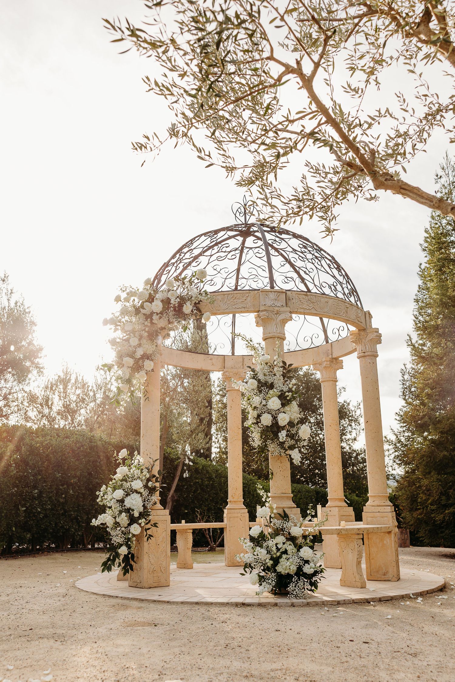Elegant white gazebo in Paso Robles decorated with white floral arrangements and greenery in a garden setting at sunset.