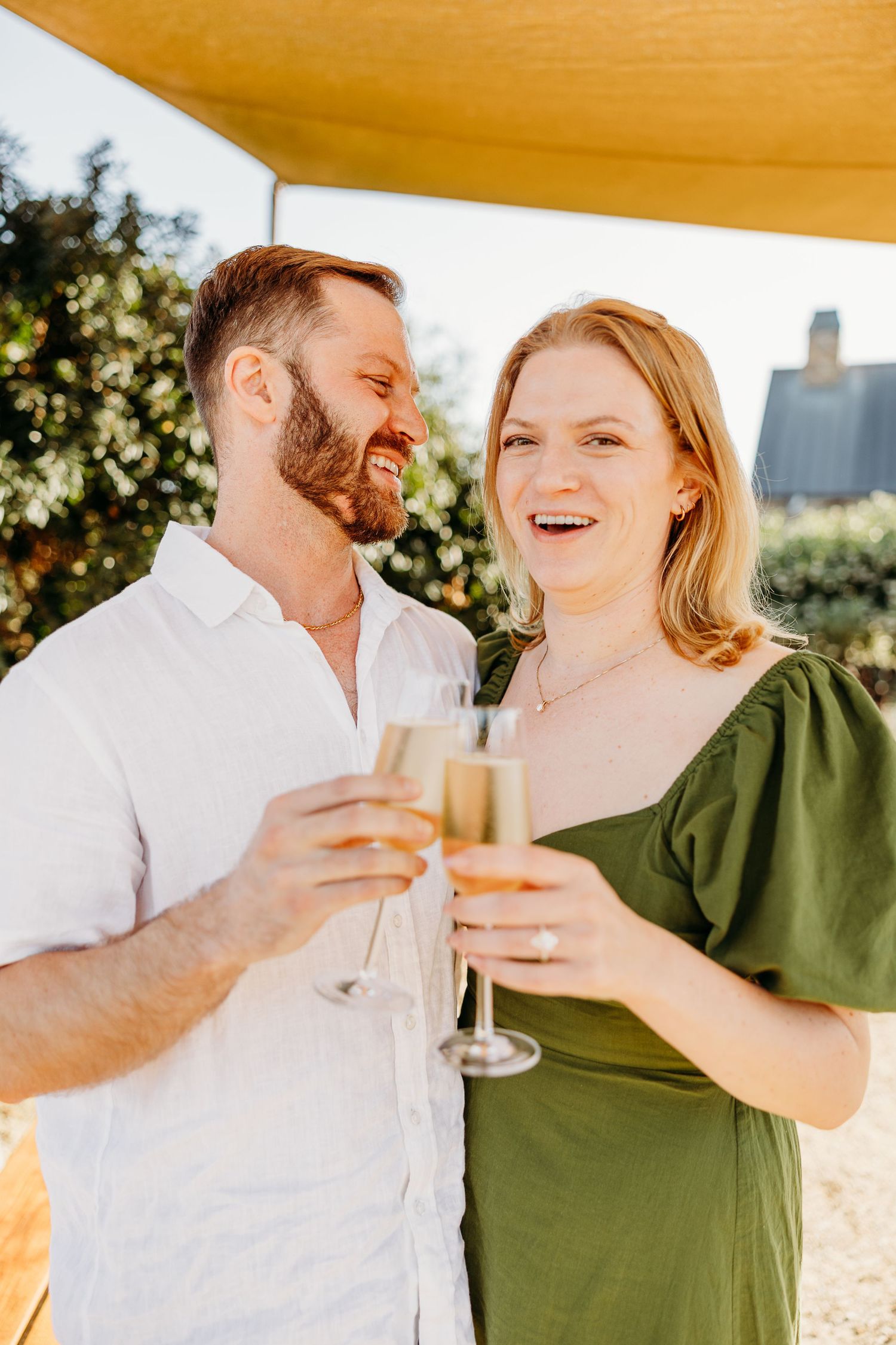 Two people toasting with champagne glasses under a golden canopy at sunset.