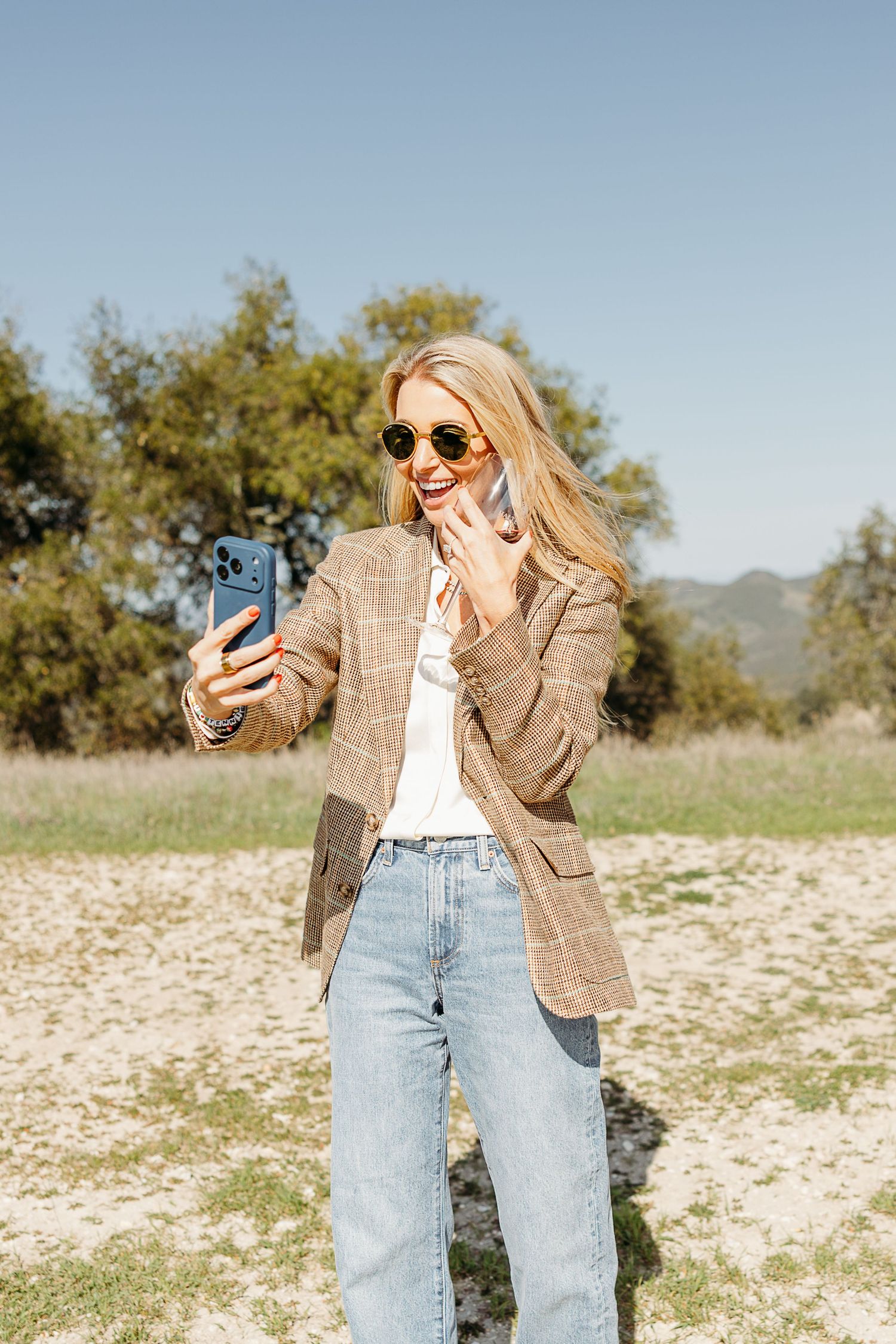 Casual fashion photo series showing someone in a brown blazer and jeans posing with a phone in an outdoor field setting.
