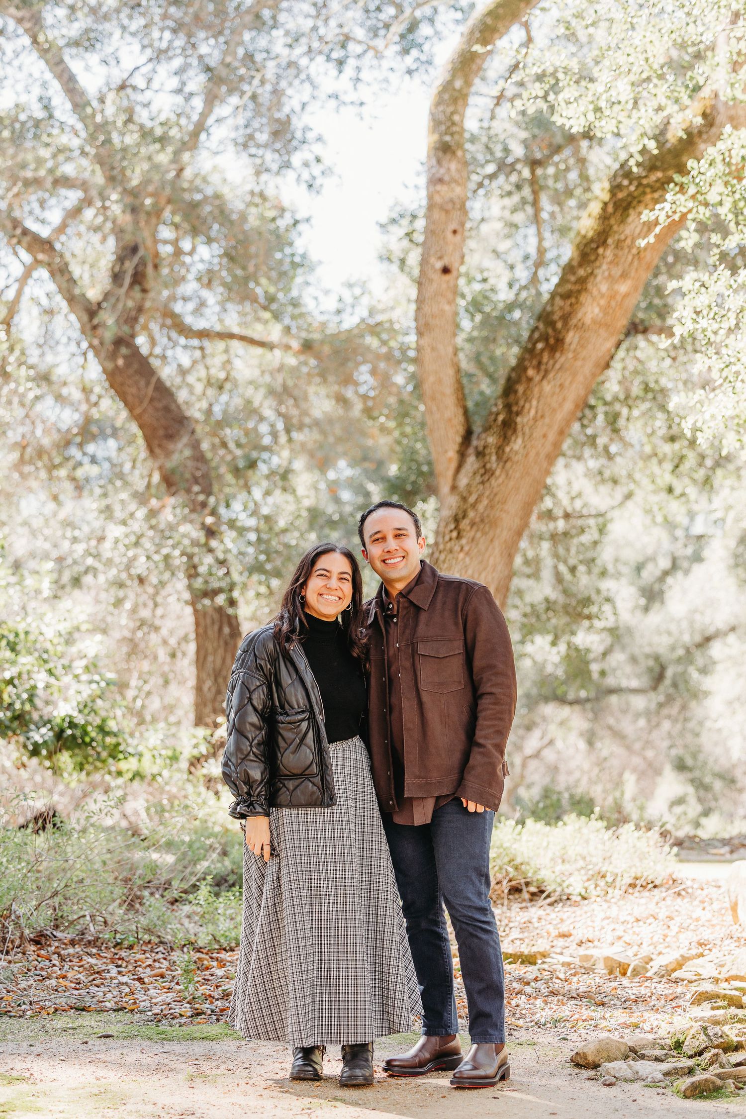 A couple poses together under sunlit trees in a romantic outdoor photoshoot.