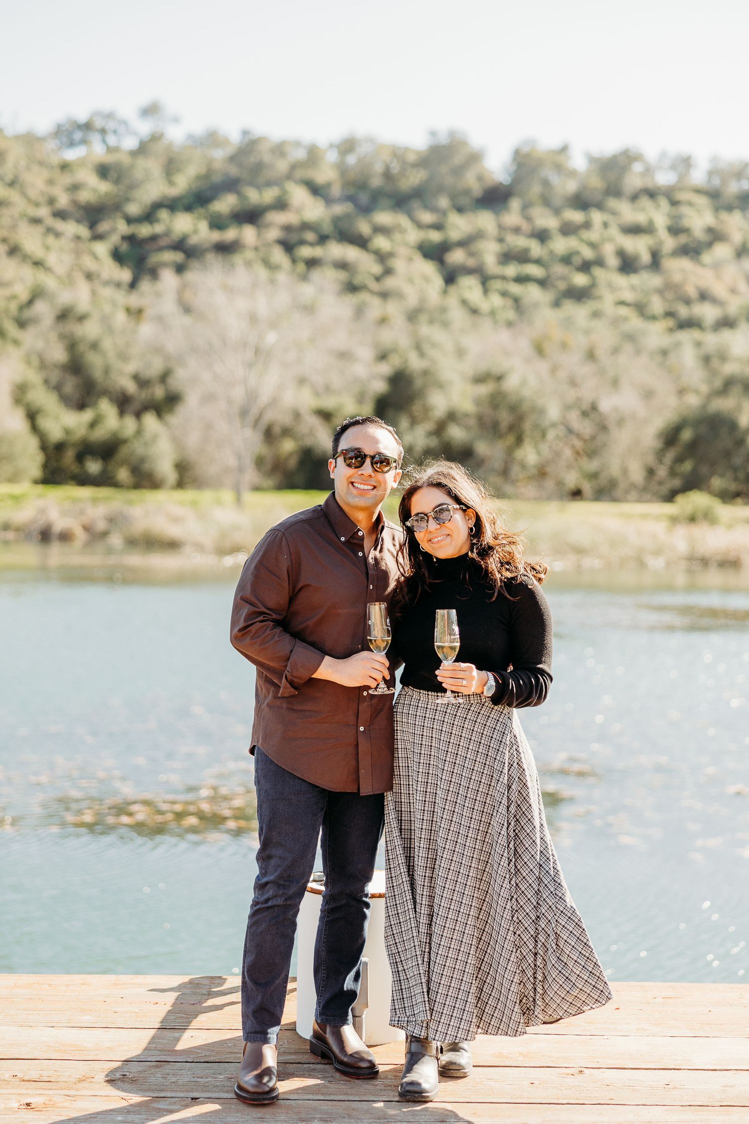 A couple sits together on a wooden dock overlooking a serene lake.