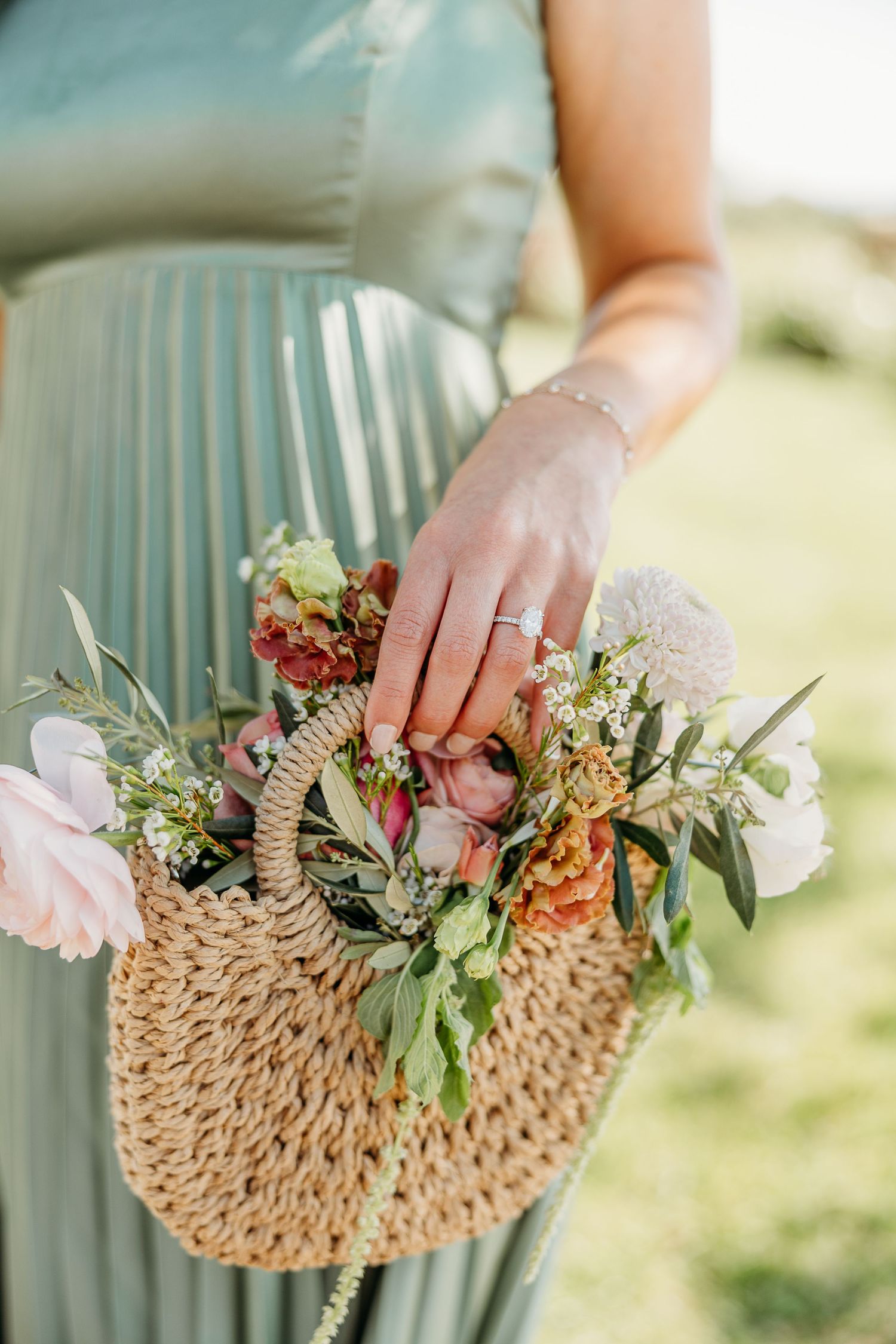 Hands holding a rustic woven straw clutch purse adorned with delicate pink and peach flowers and greenery.