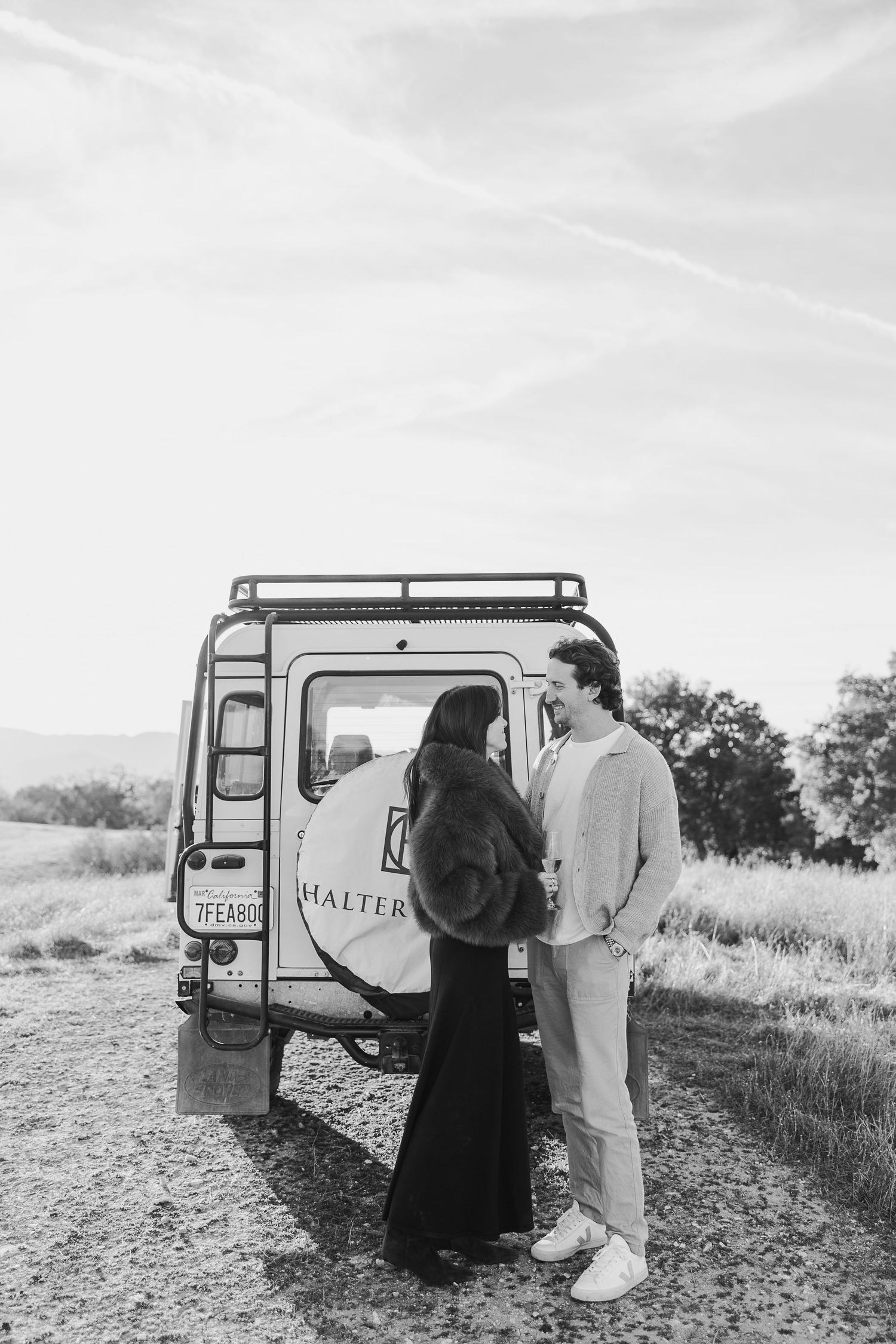 Couple standing next to a Land Rover vehicle in an open field during a photoshoot.