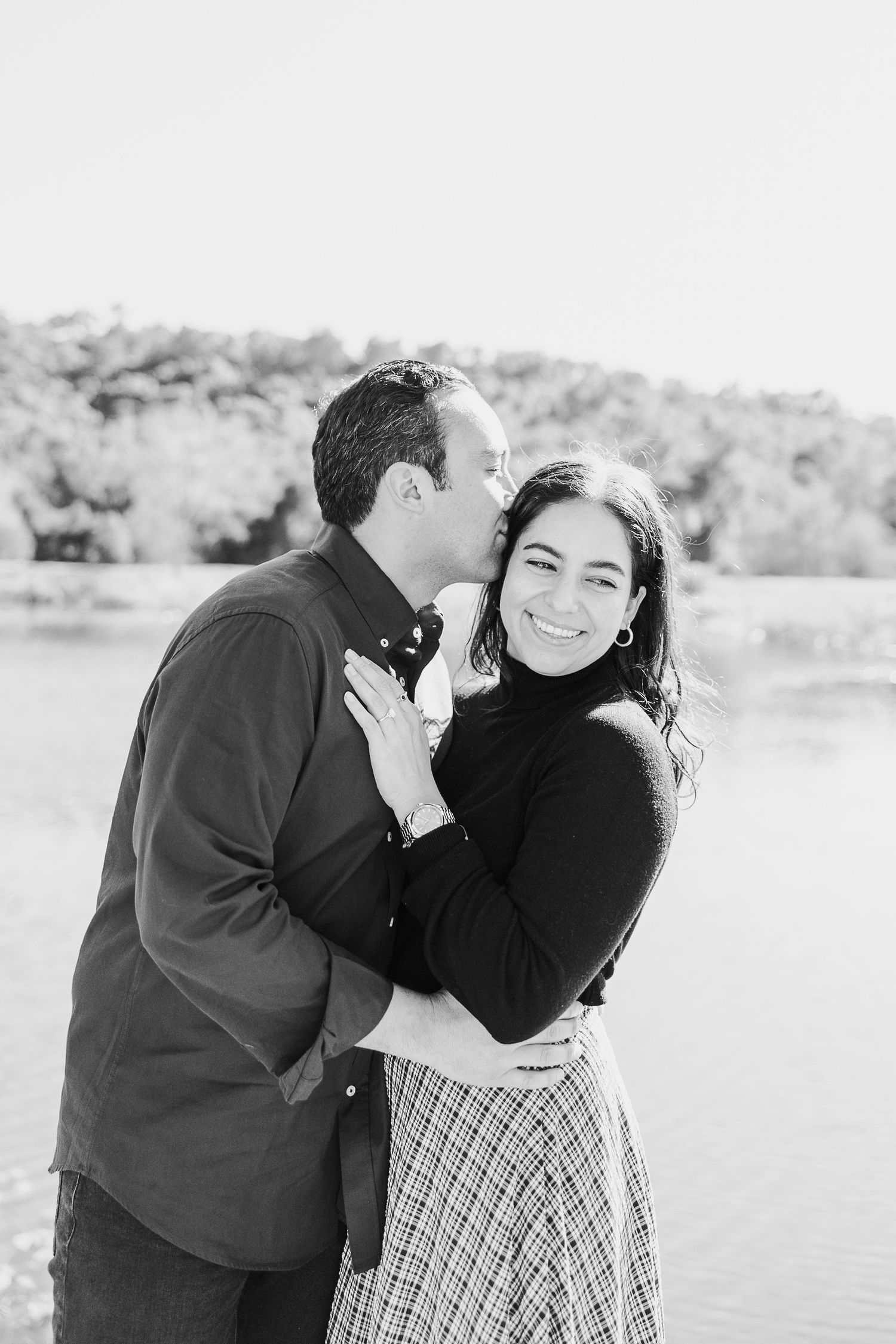 A couple shares an intimate moment in black and white photography by the water.