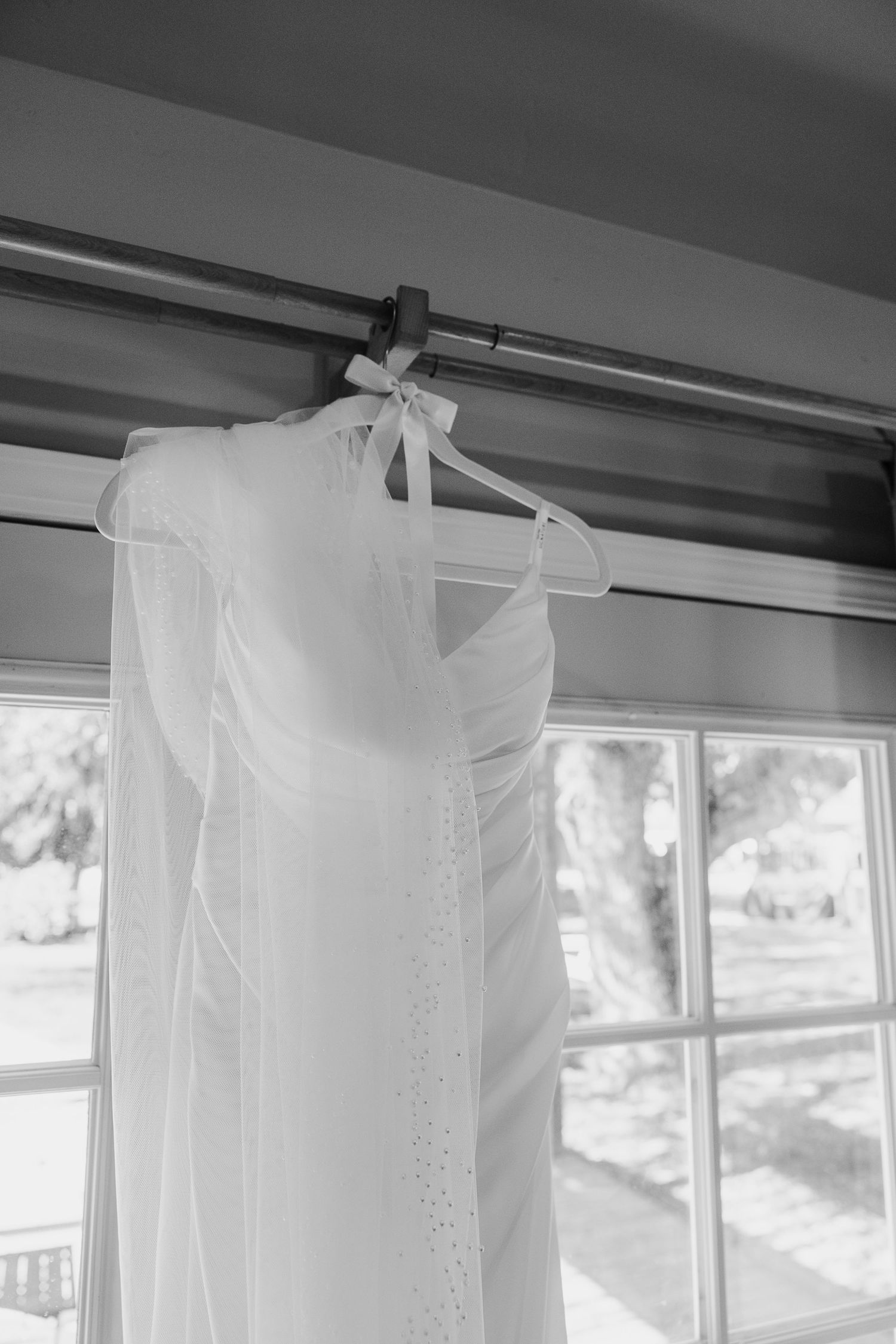 White wedding dresses hanging on a rack against bright windows in a bridal boutique.