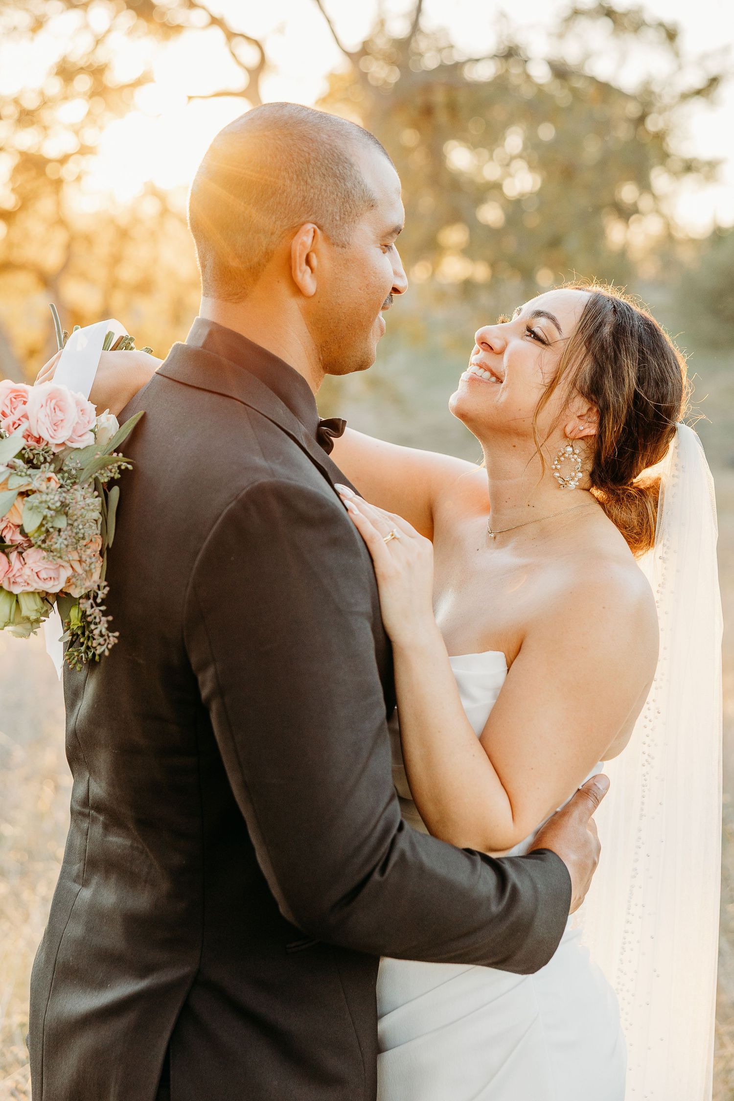 A romantic wedding couple embraces in golden sunlight while sharing a joyful moment together.