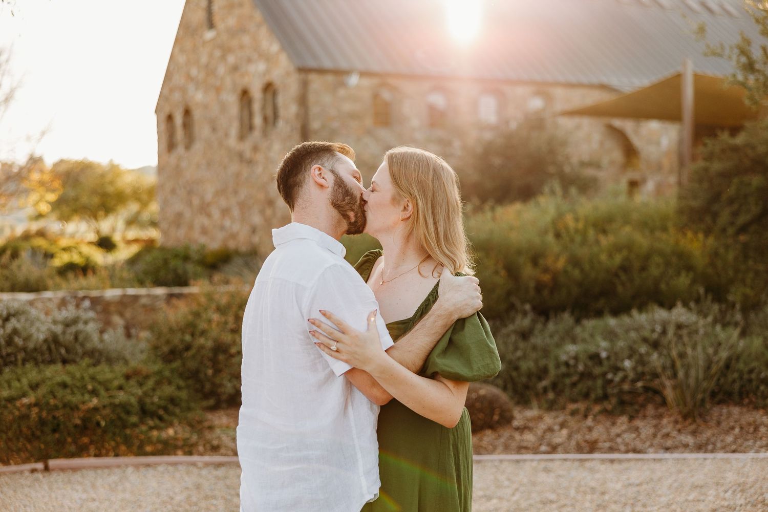 A couple embracing during golden hour at a winery with stone walls.