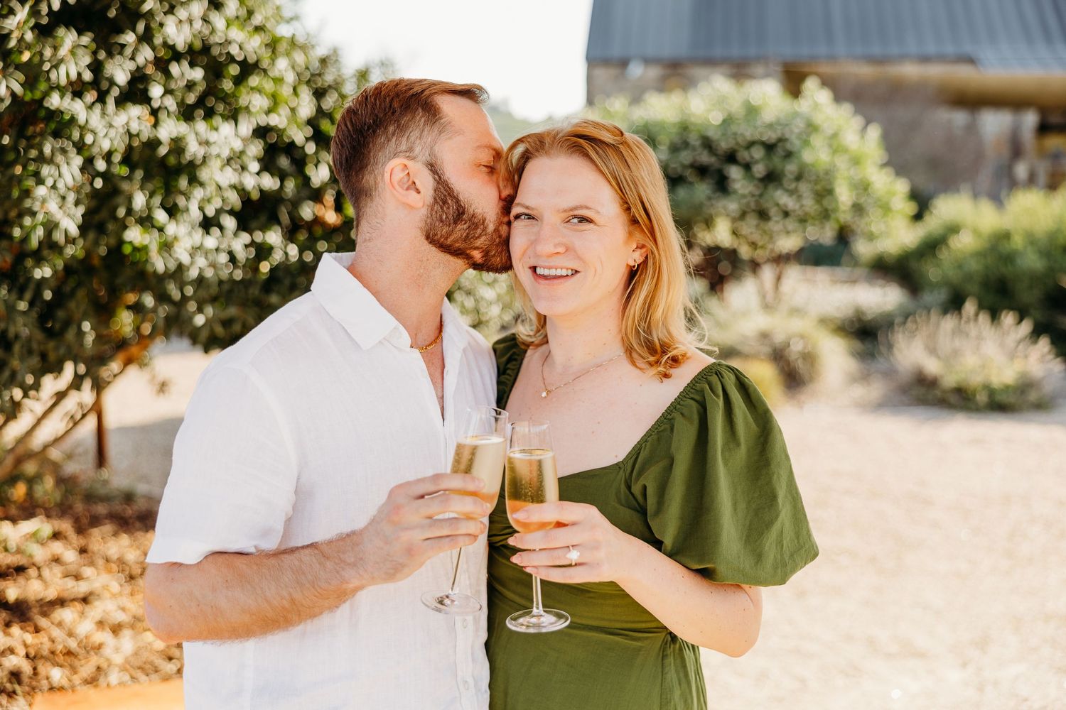 A romantic couple shares champagne and intimate moments in a sunny outdoor setting with natural lighting.