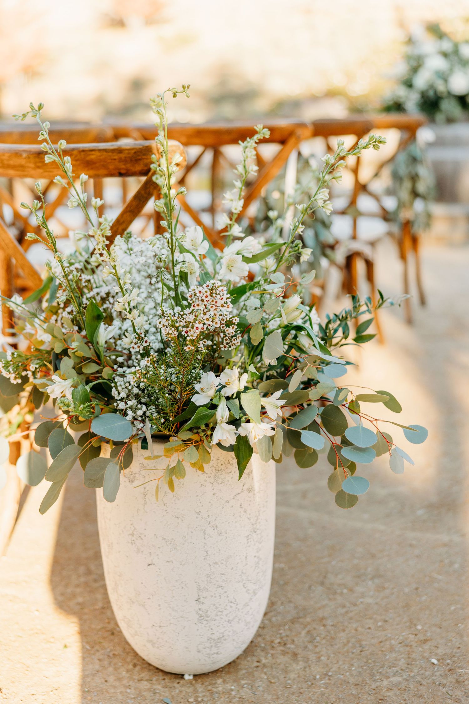 White floral centerpieces with eucalyptus in concrete vessels lined up on a table.