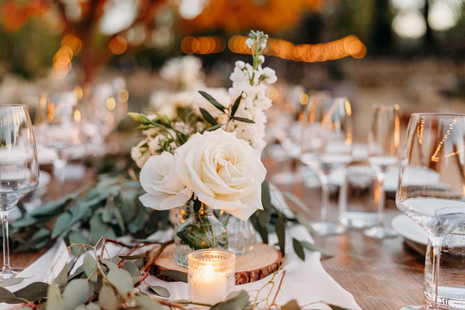 Elegant wedding table setting with white roses, greenery, and candlelight creating a romantic atmosphere.