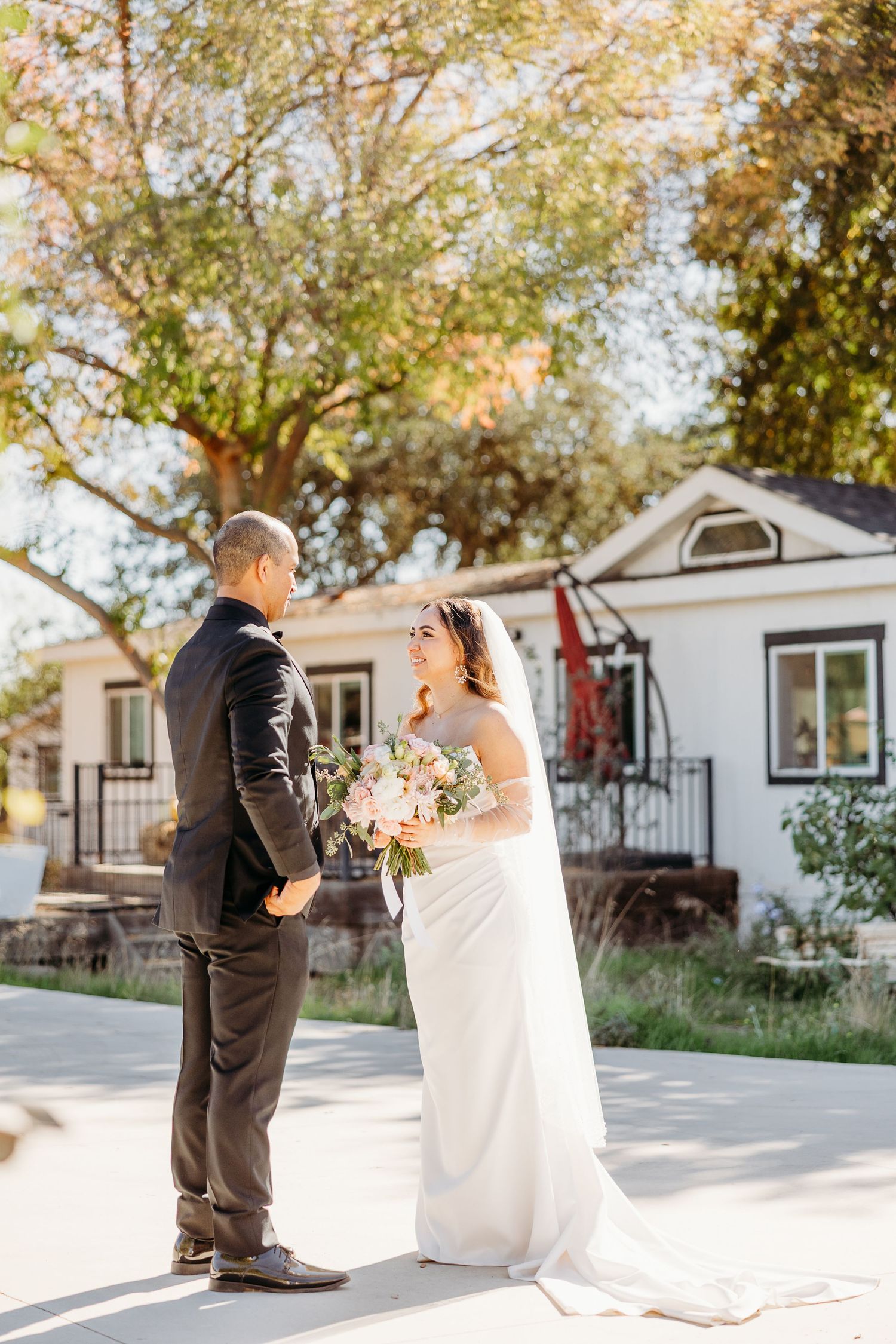 Outdoor wedding ceremony with couple standing together in front of a white house on a sunny day.