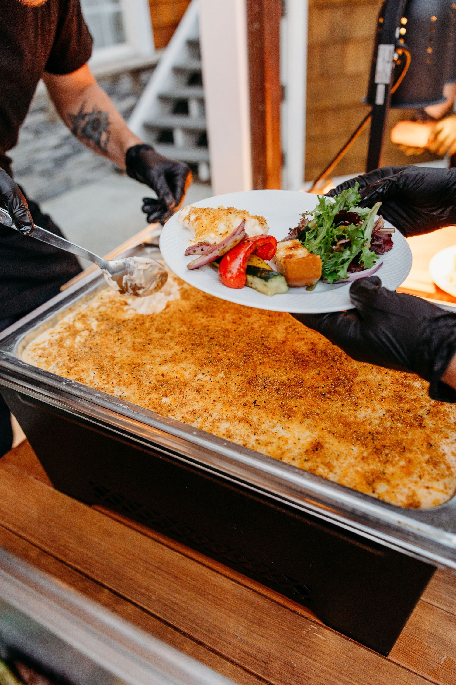 Catering staff preparing large pan of golden-brown baked dish for service.