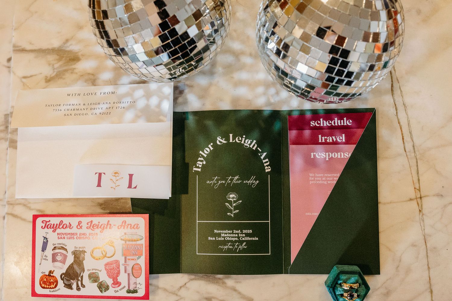 Shiny disco balls hang from the ceiling above elegant wedding invitation cards displayed on a rustic surface.