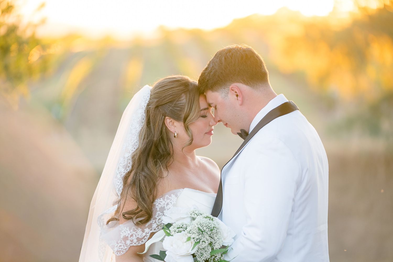 Bride and groom share romantic golden hour moment in field, bride wearing lace gown and veil.