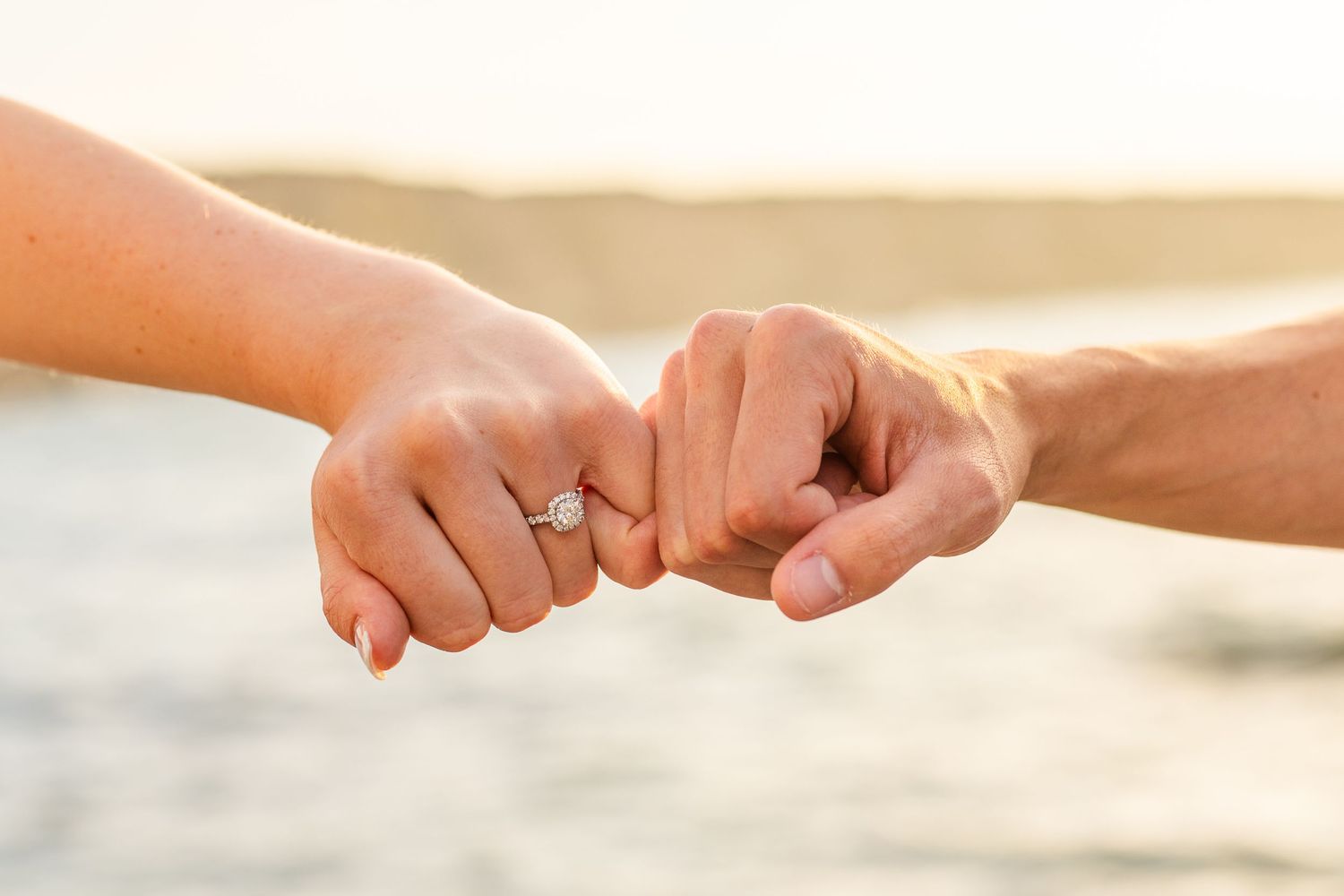 Close up of hands with an engagement ring touching on a sunny beach.