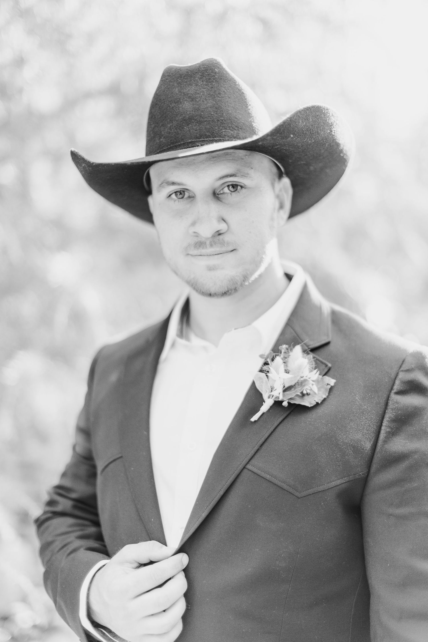 Black and white portrait of groom wearing cowboy hat and suit with boutonniere.