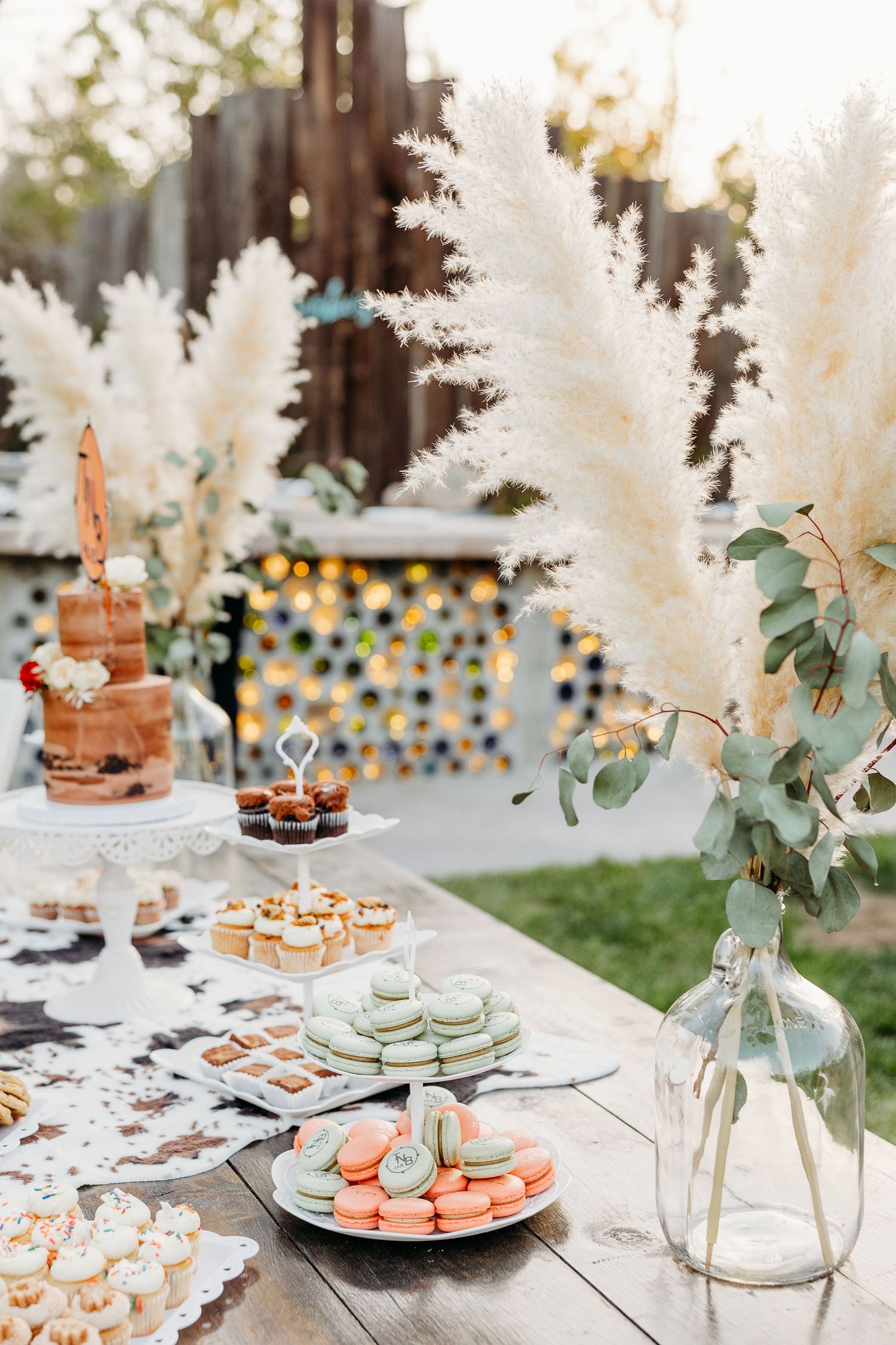 Elegant dessert table with pampas grass decorations and macarons on tiered stands.