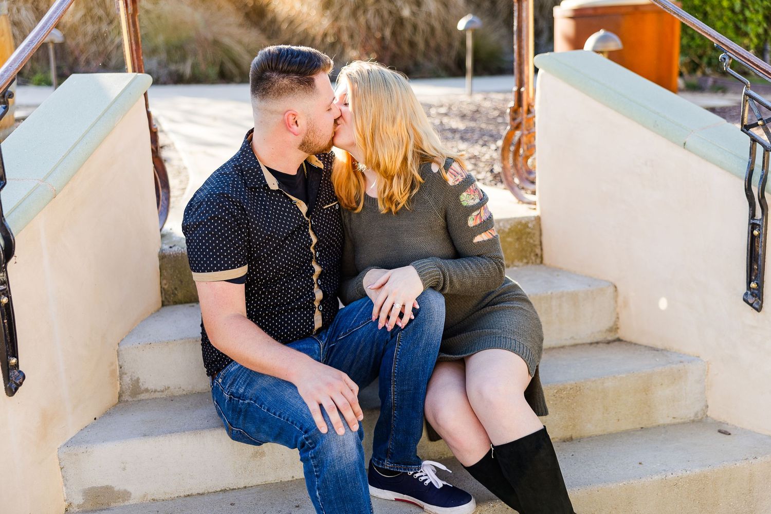 A couple shares an intimate moment while sitting on concrete steps outdoors.