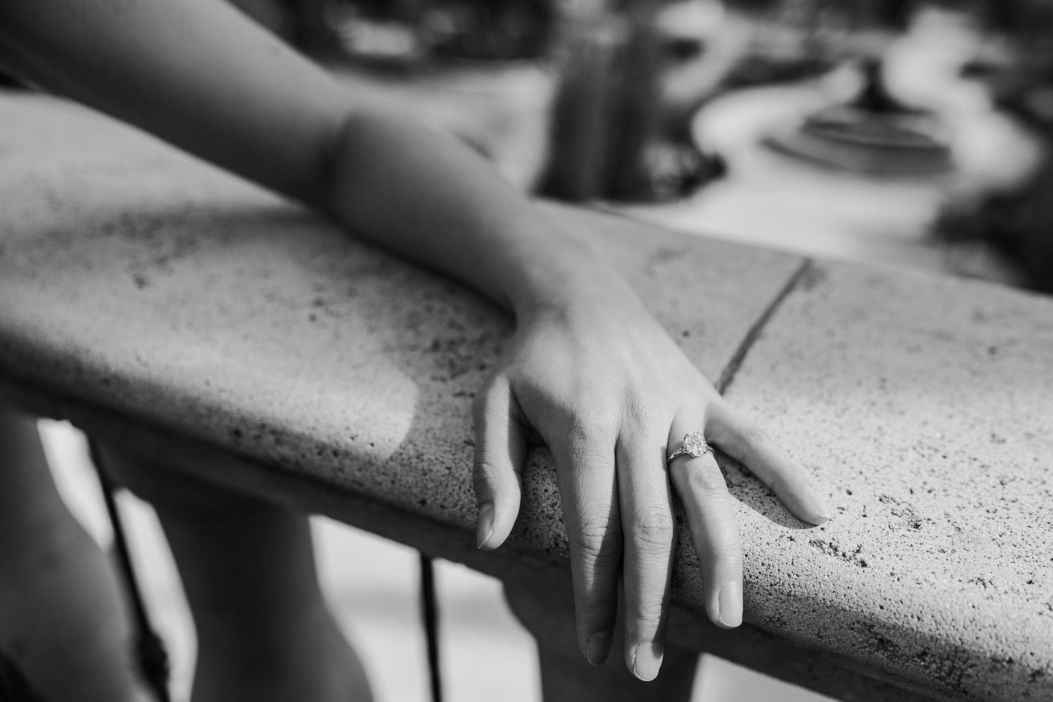Close-up black and white photo of a hand resting on a stone railing.